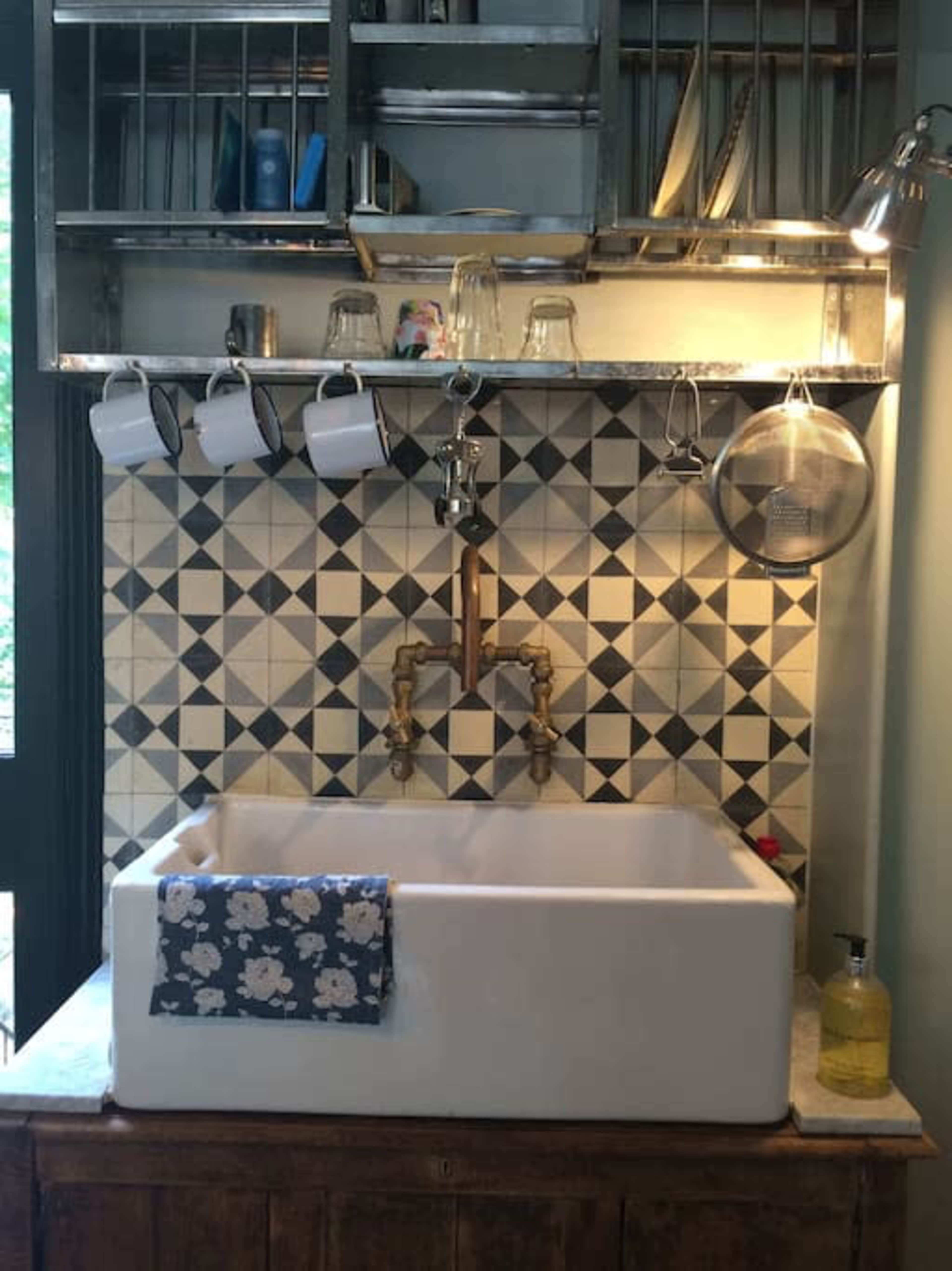 A kitchen sink with a white ceramic basin, a wall-mounted faucet, and a tiled backsplash featuring a geometric pattern.