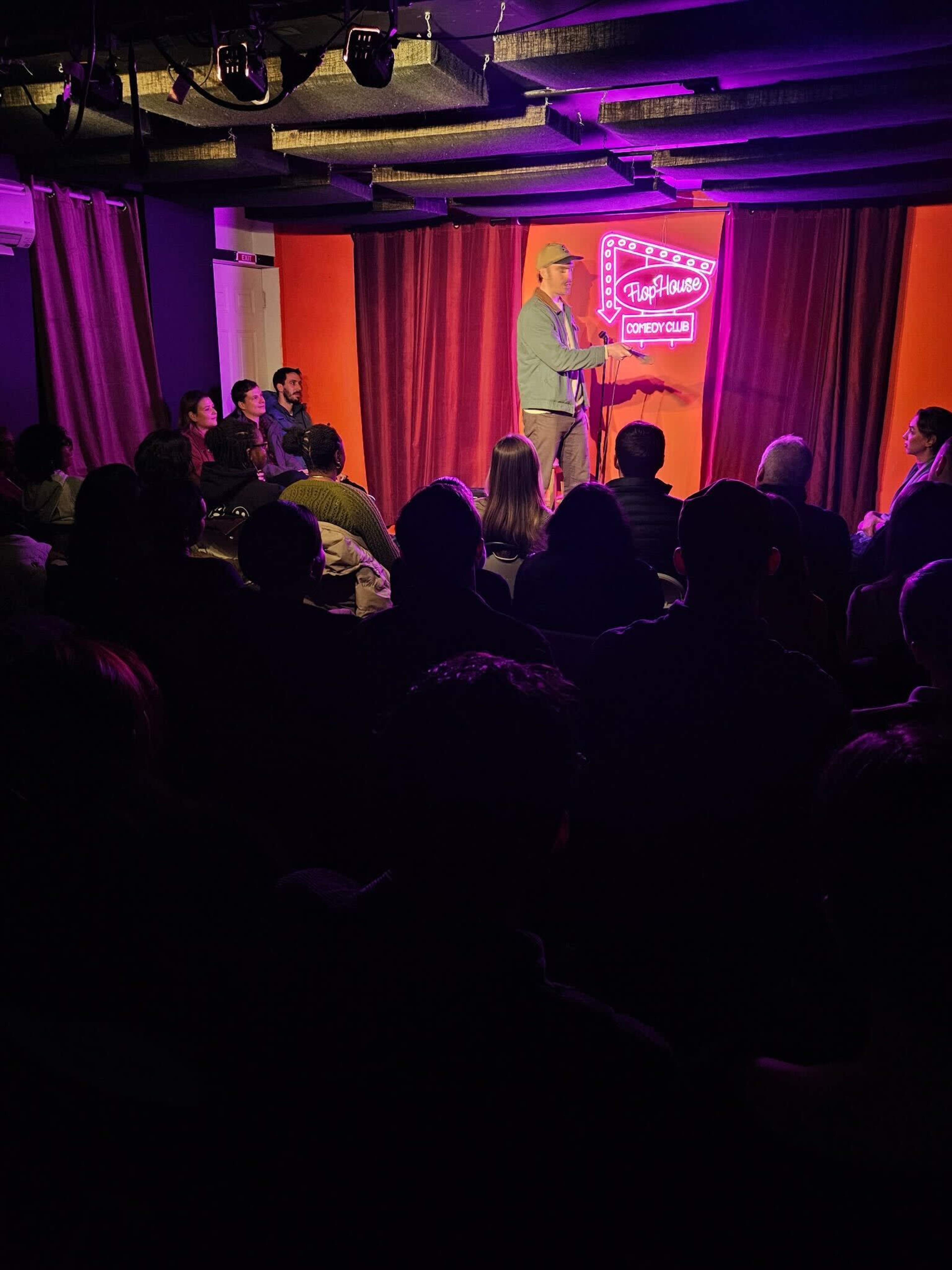 A comedian performs on stage at a comedy club while an audience watches attentively.