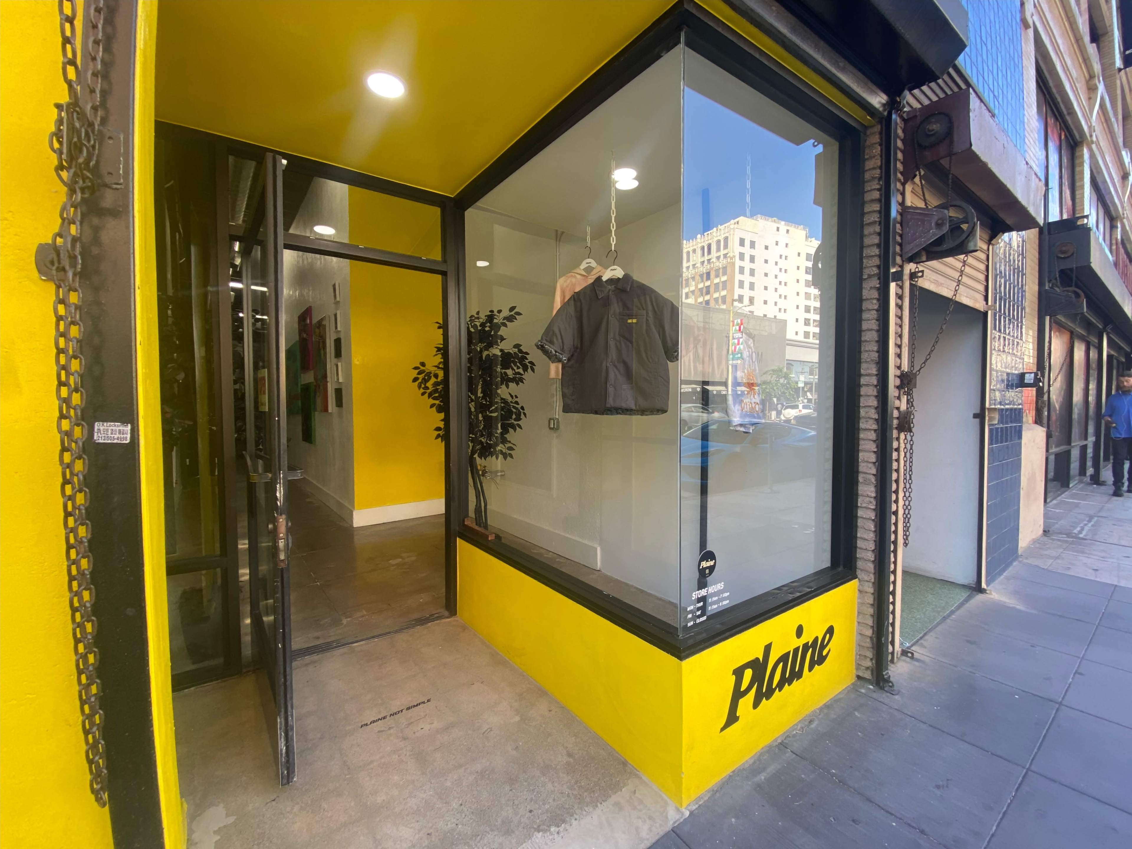 The image shows a clothing store named "Plaine" with a yellow exterior and a clear display window showcasing garments.