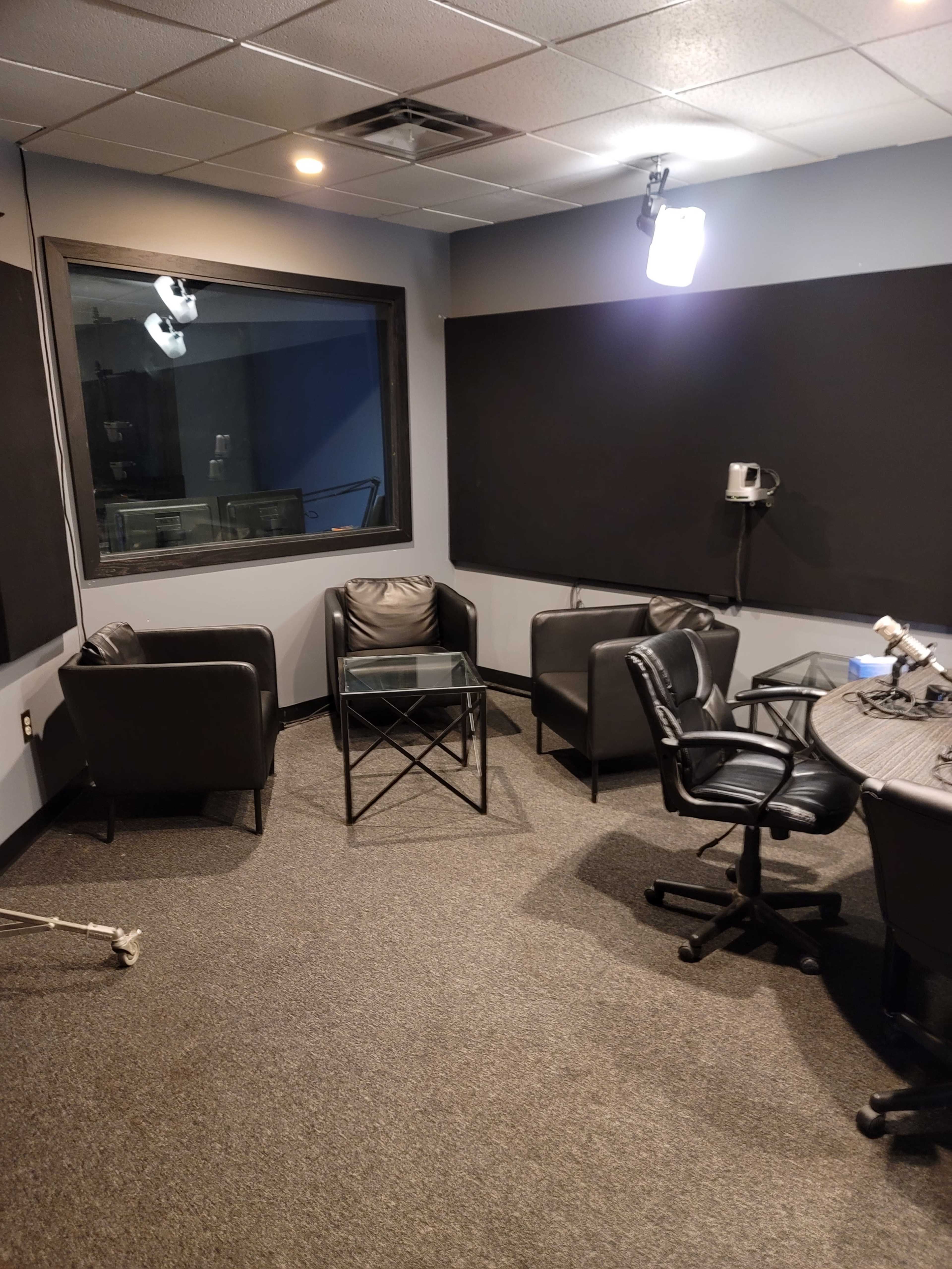 A small recording studio with two black chairs and a glass table arranged on a gray carpet.