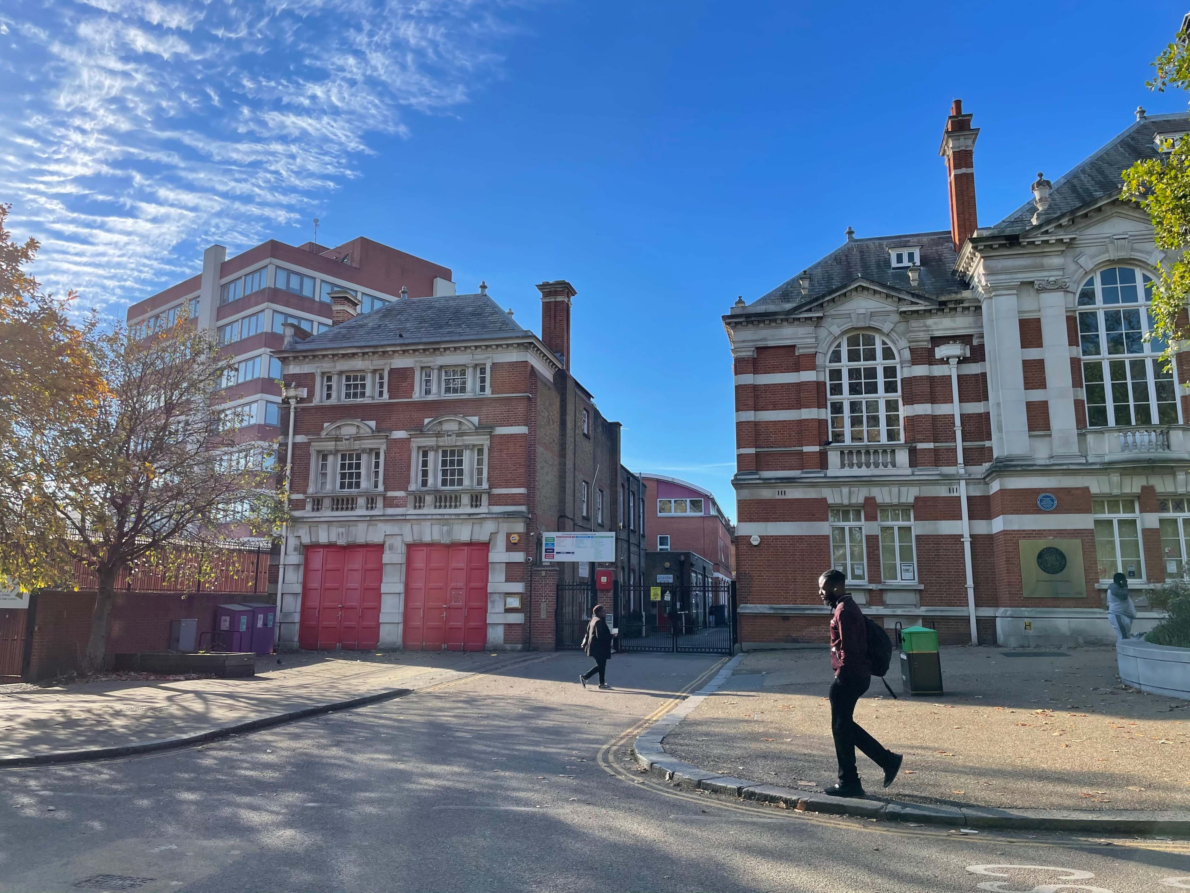 A street scene featuring two distinct buildings, one with large windows and red brickwork, and another with a red garage door, under a clear blue sky.