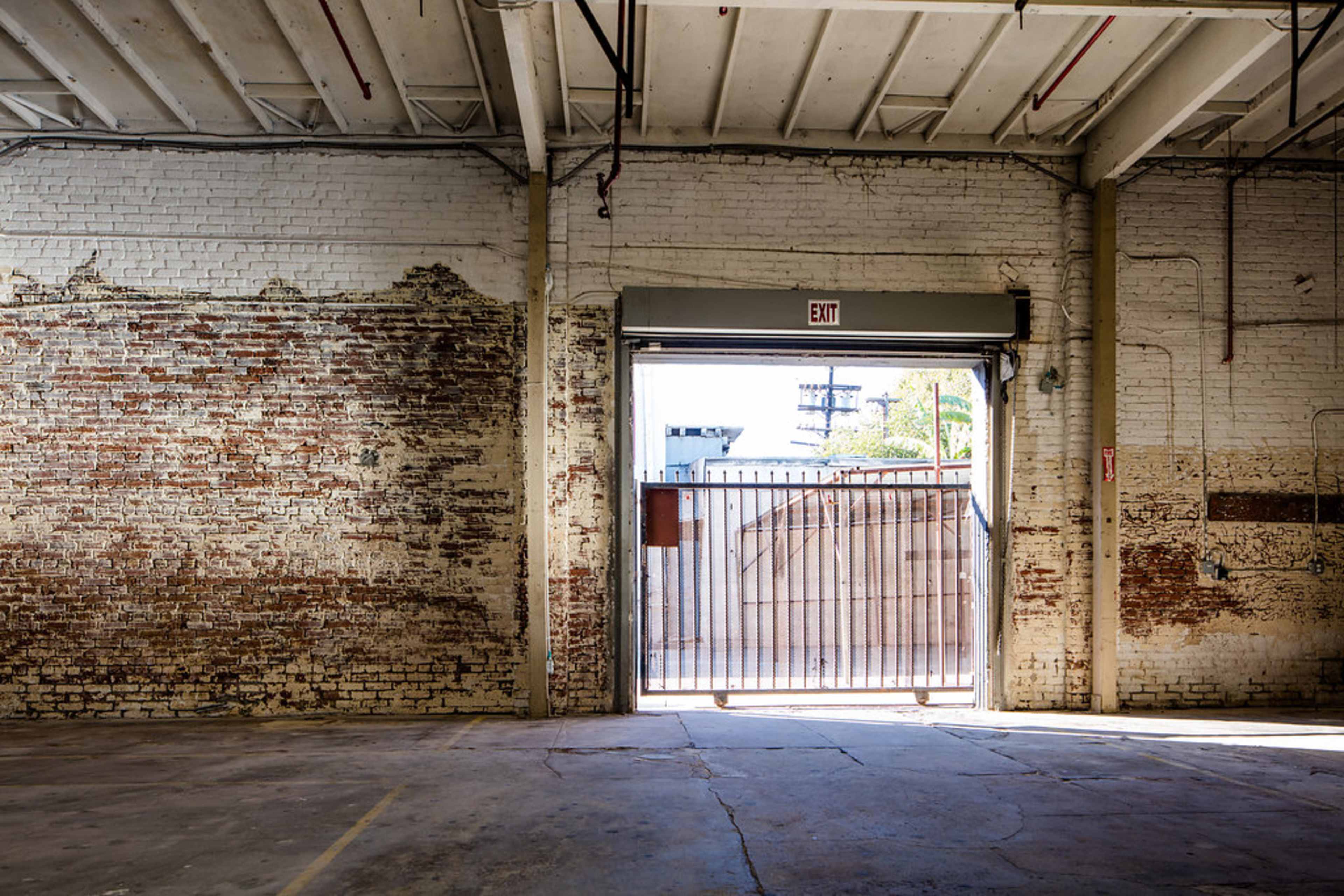 The image depicts a spacious industrial interior with exposed brick walls and a large open doorway leading to an exterior area.