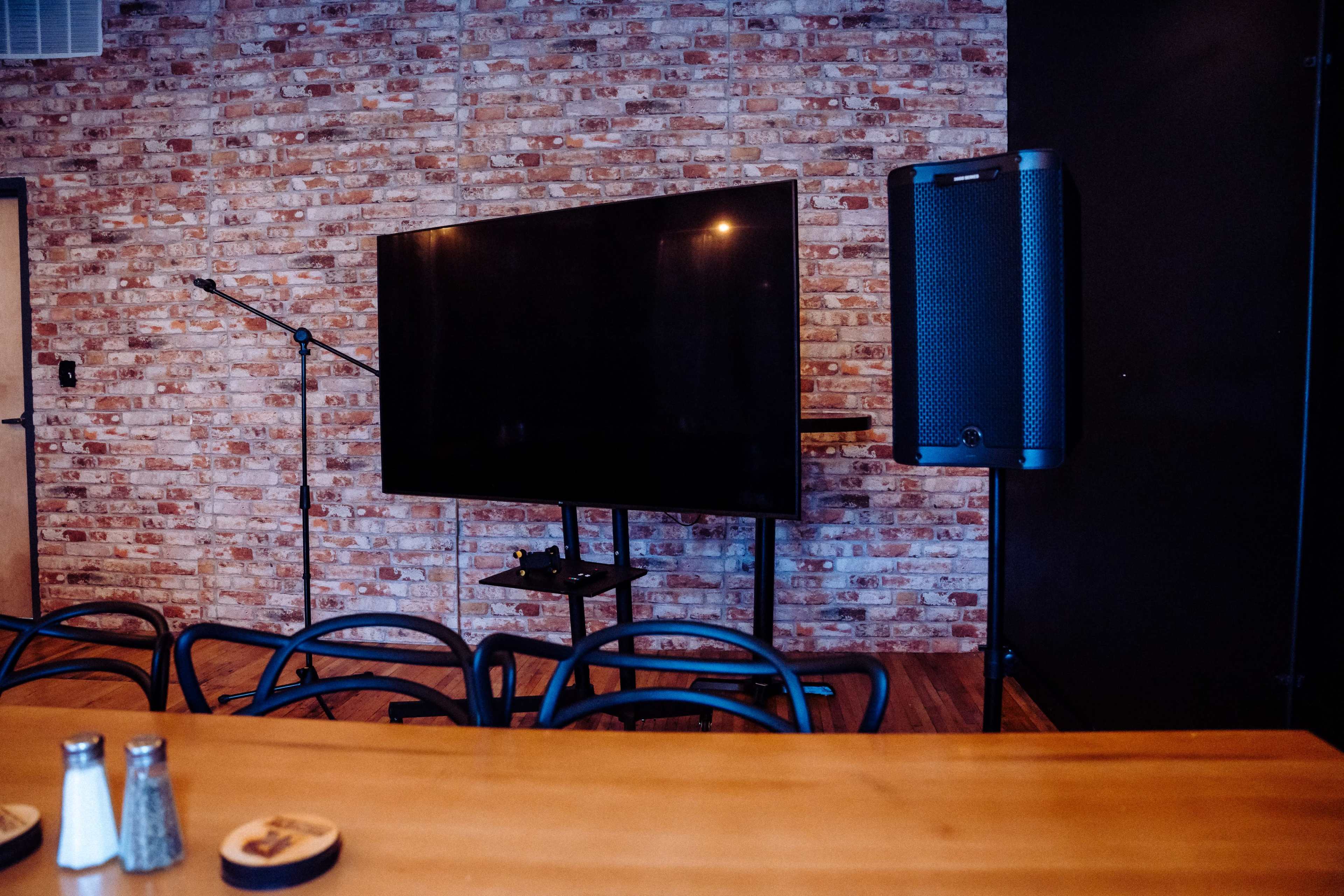 A modern room features a large television mounted on a stand against a brick wall, accompanied by a microphone and a speaker.
