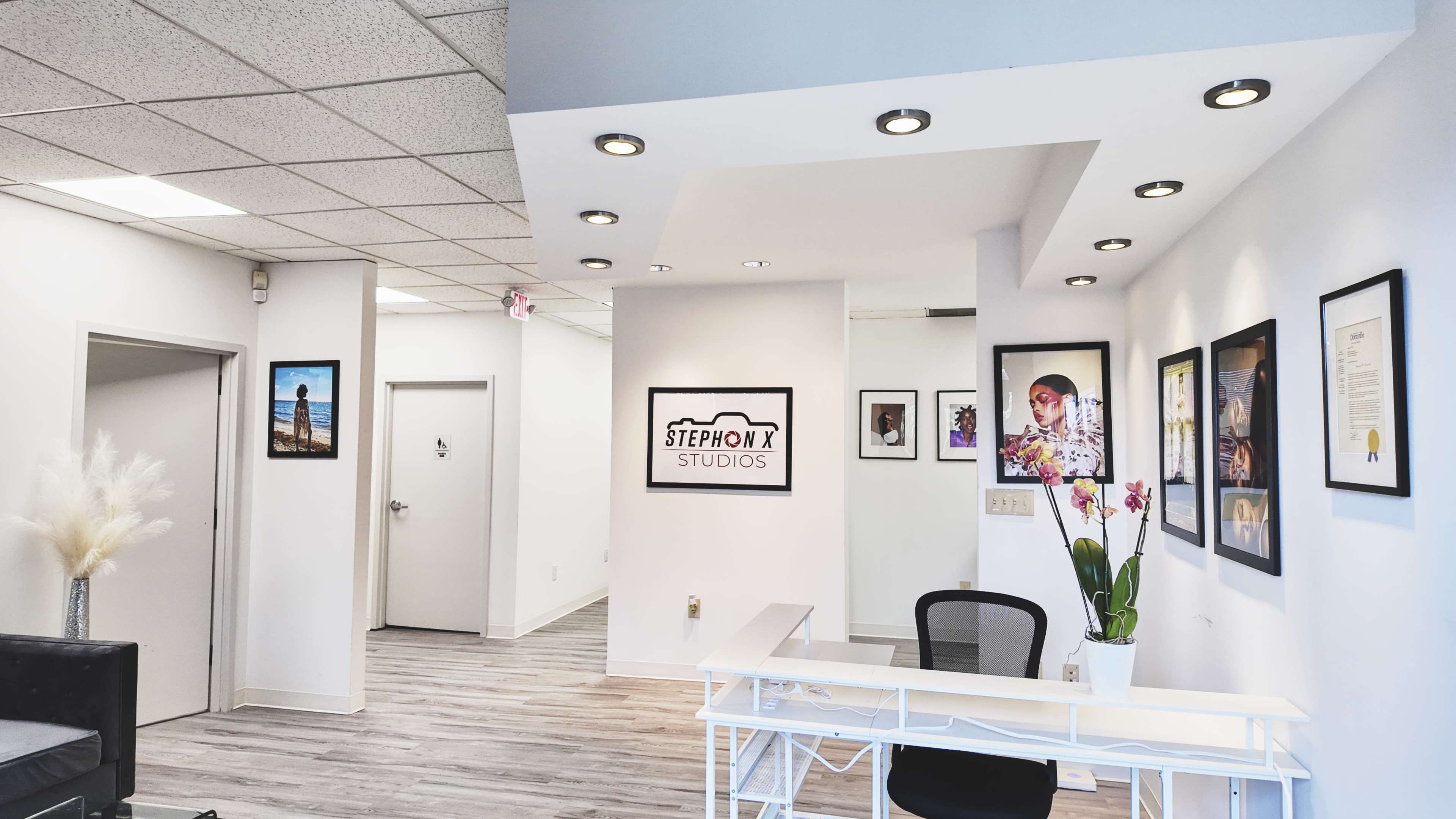 A modern studio interior featuring a reception area with a white desk, framed art on the walls, and a potted orchid.