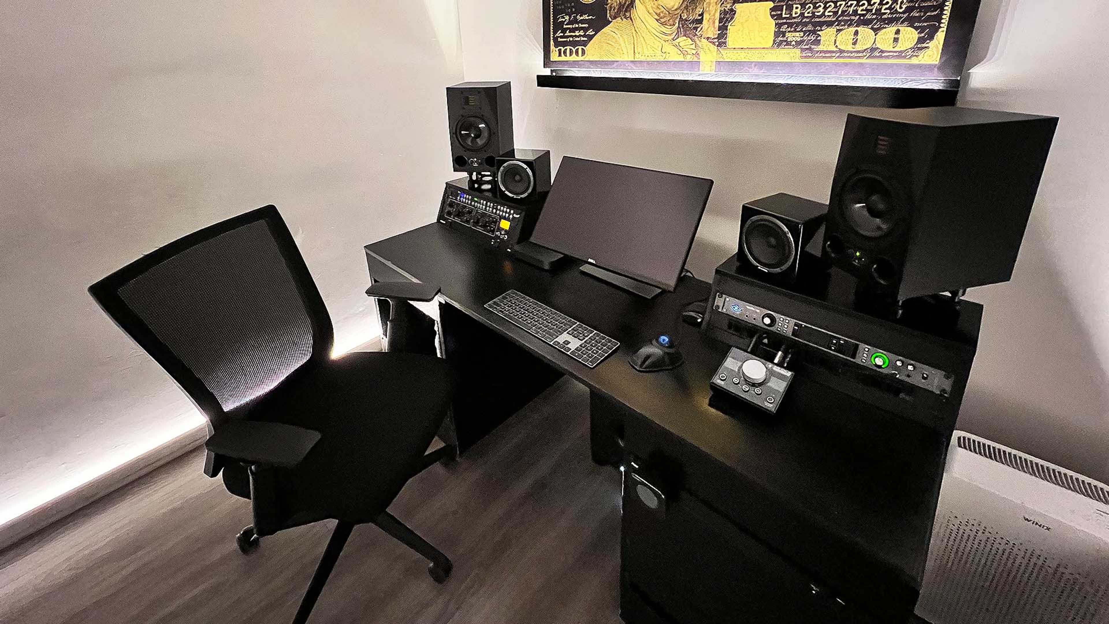 A modern computer workstation with a black desk, a monitor, audio speakers, and a rolling office chair.