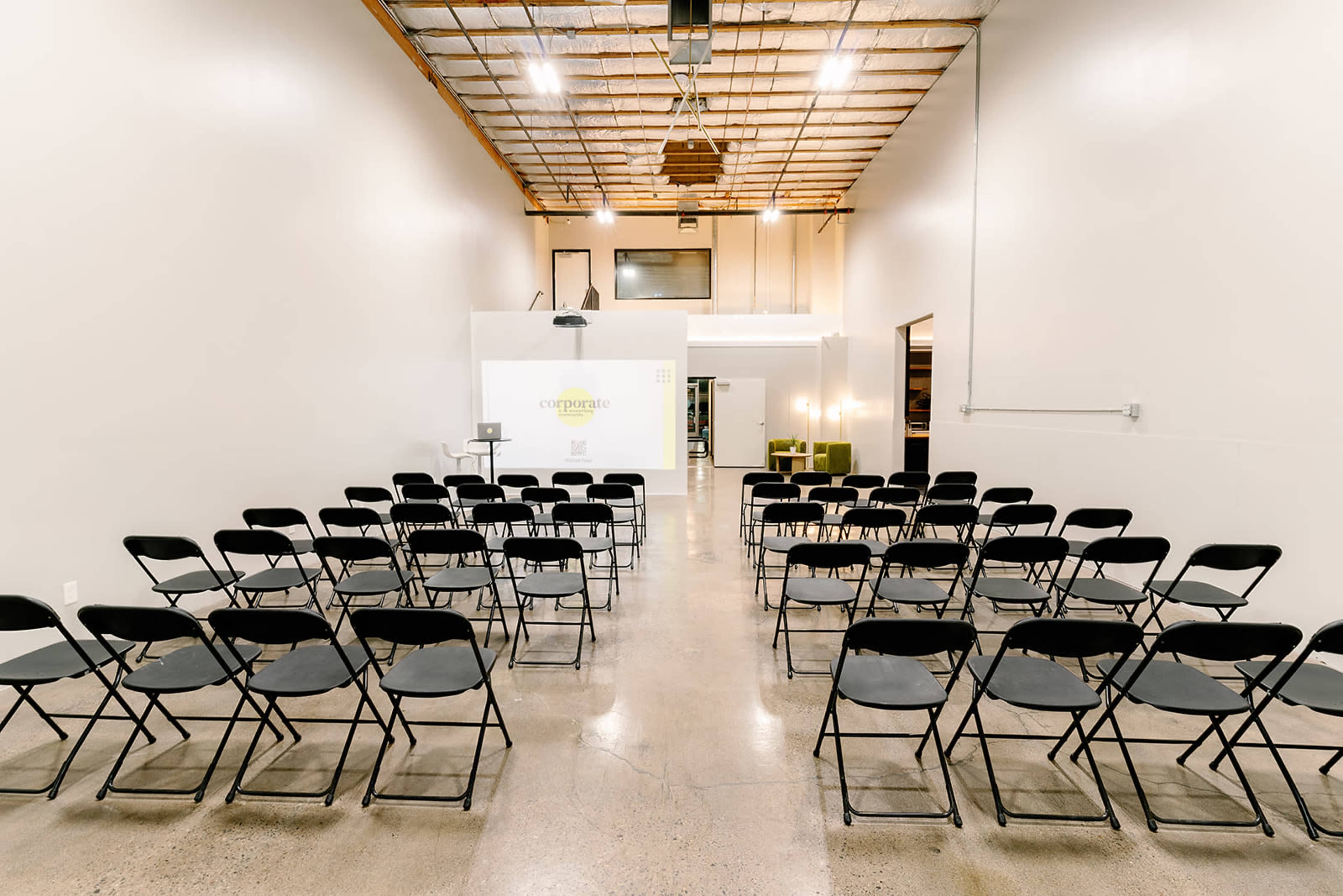 A spacious room set up with rows of black folding chairs facing a presentation screen.