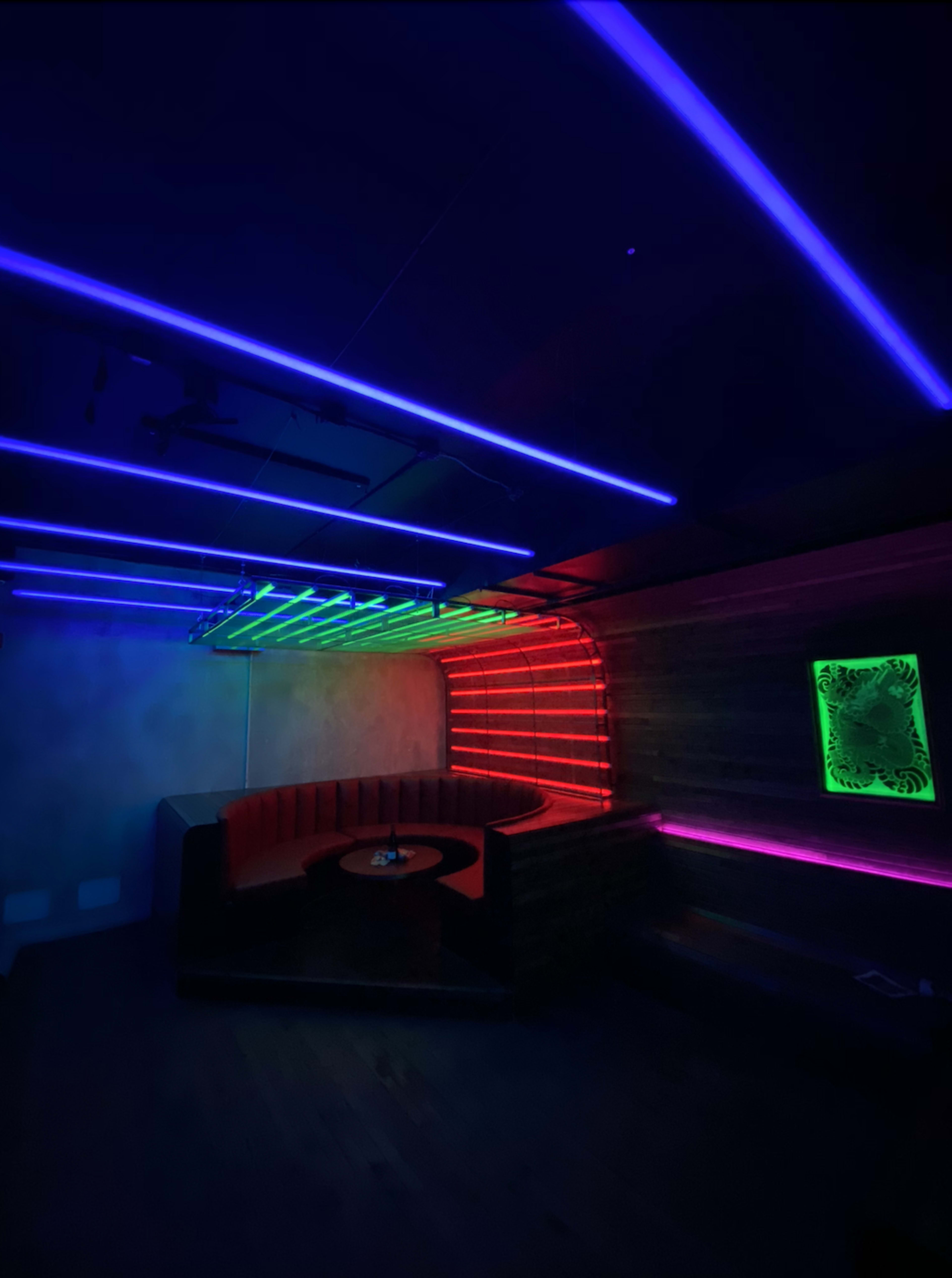 The image shows a dimly lit room with vibrant neon lights in blue, green, and purple illuminating the walls and ceiling.