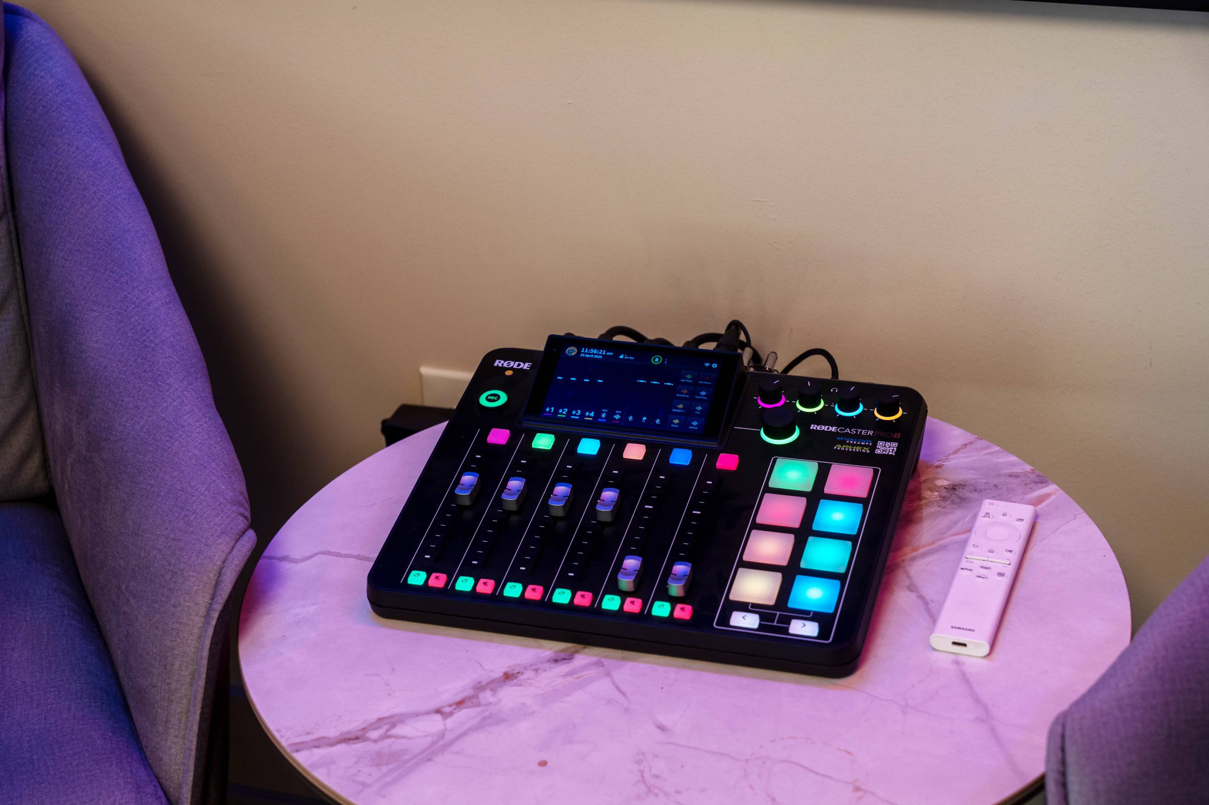 A multimedia mixing console with various colored buttons and faders is placed on a marble-topped table next to a remote control.