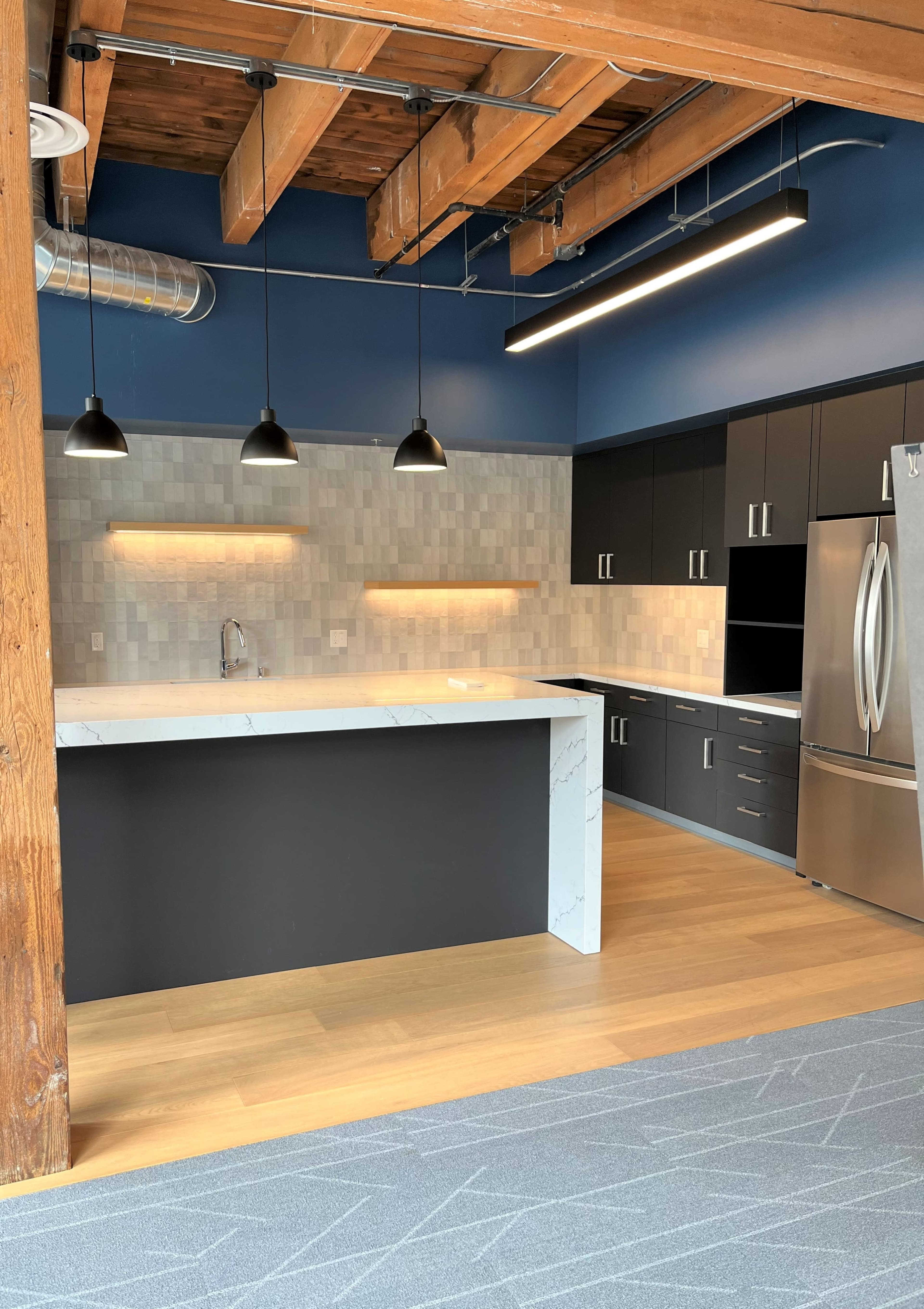 The image shows a modern kitchen with dark cabinetry, a marble-topped island, and exposed wooden beams above.