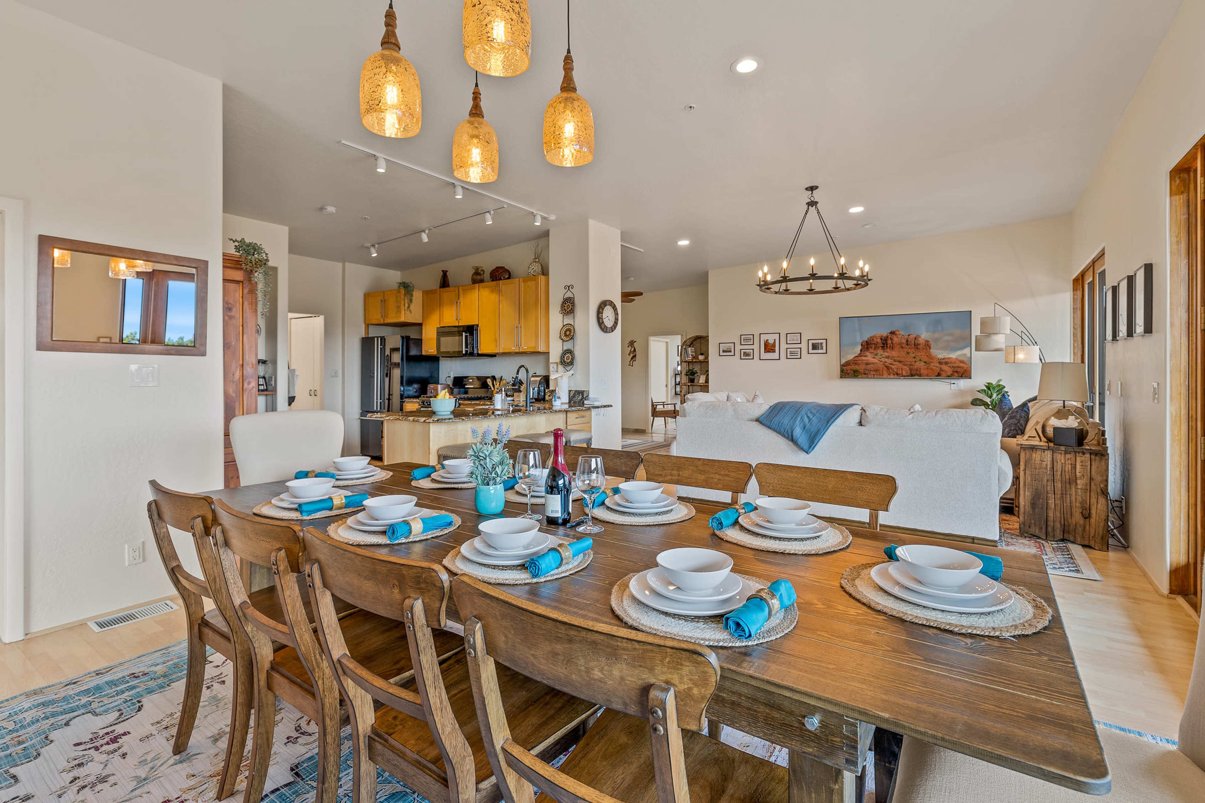 A dining table is set with plates and utensils, and a kitchen area is visible in the background with yellow cabinets and a living space featuring a couch and decorative items.