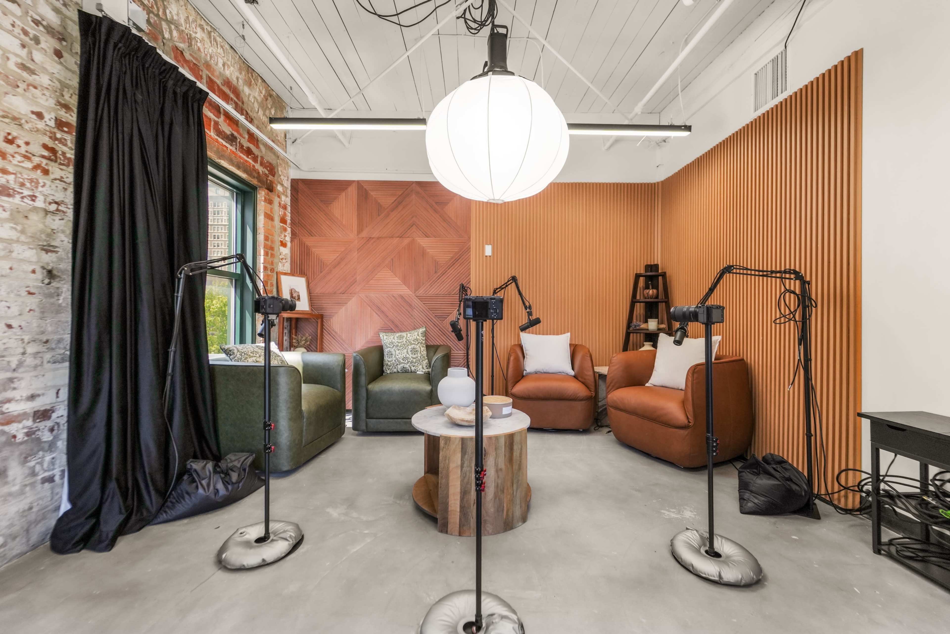 The image shows a cozy recording studio with two leather chairs, a green couch, and several microphone stands positioned around a wooden coffee table.