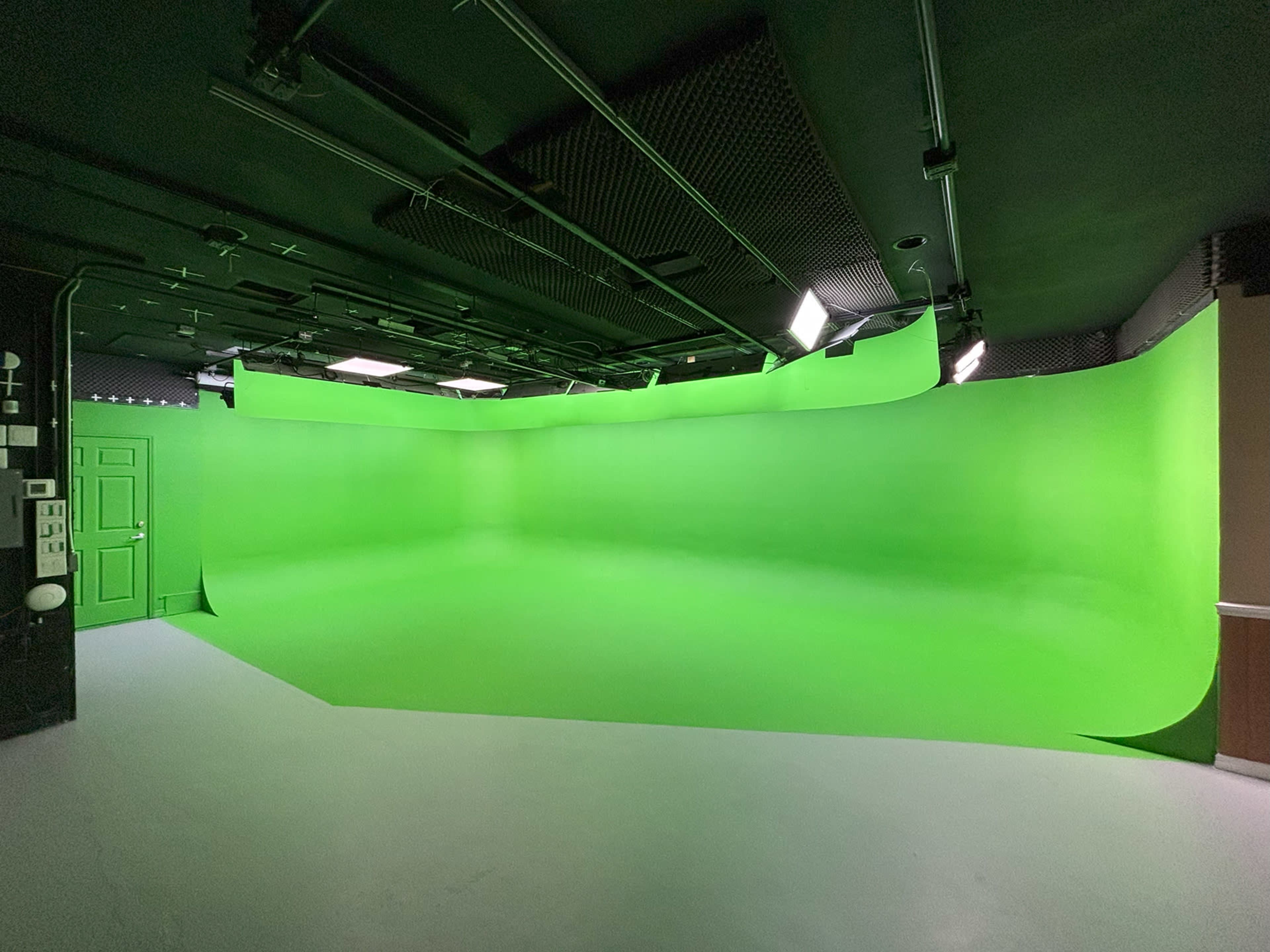 The image shows an empty green screen studio with a curved green backdrop and dim overhead lighting.