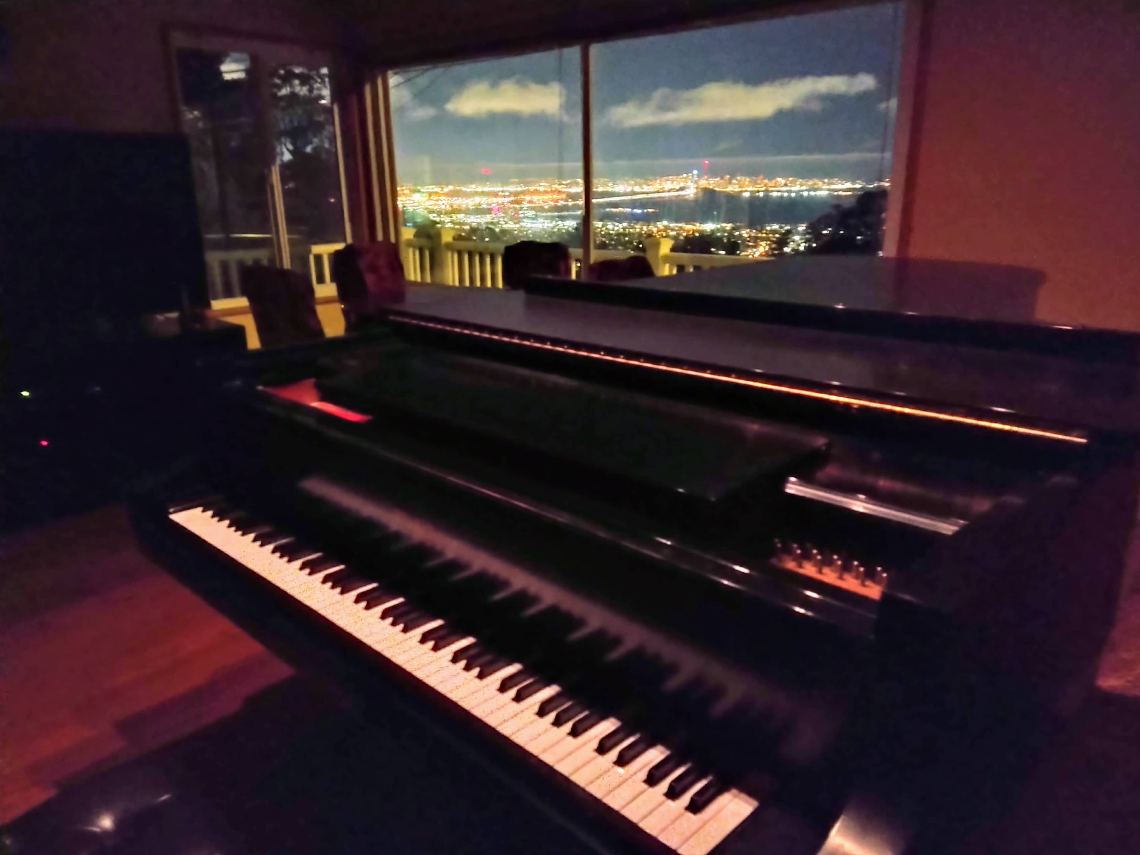 A grand piano is positioned near a large window overlooking a city skyline illuminated at night.