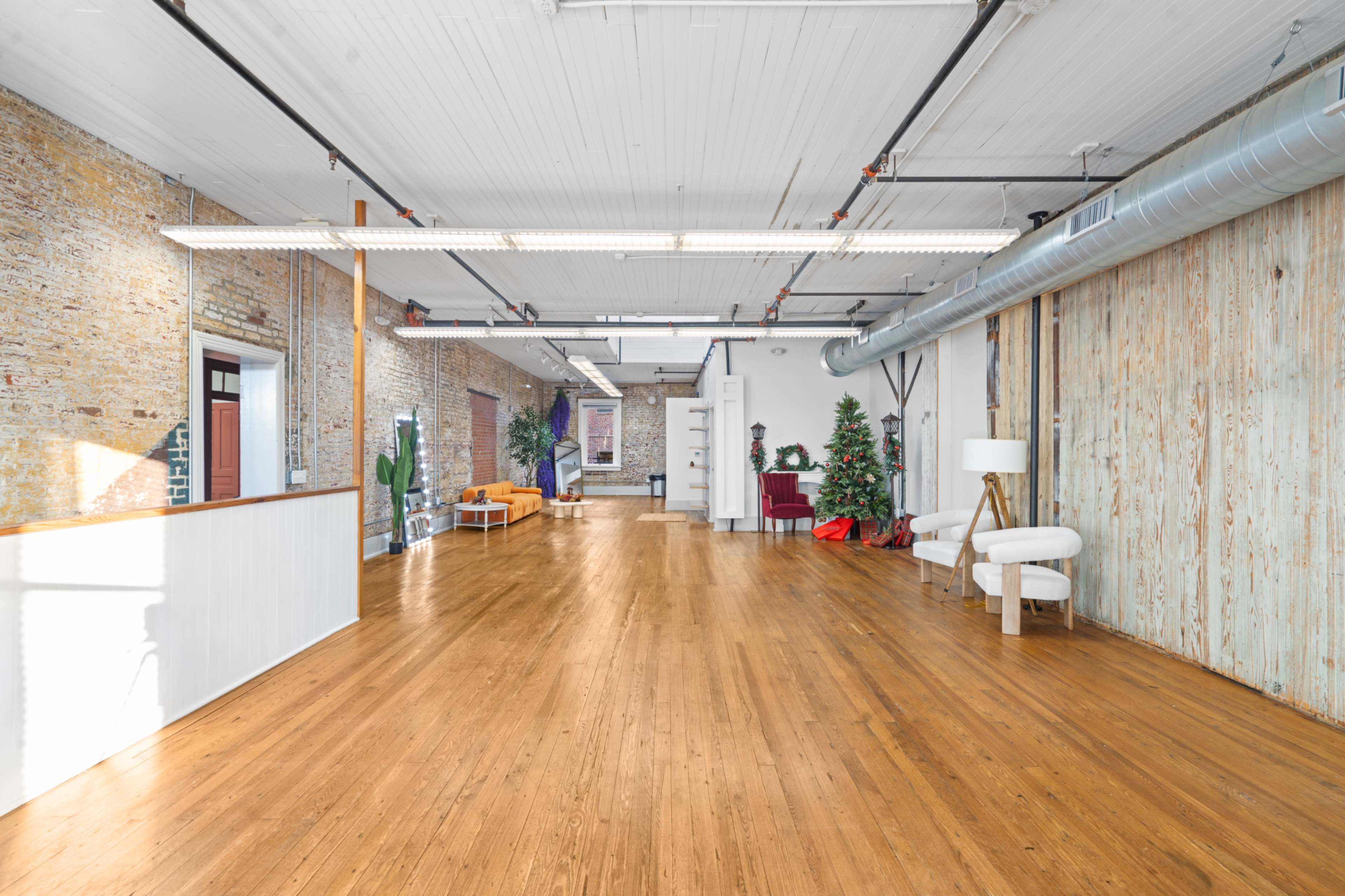 The image shows a spacious, well-lit commercial interior with wooden floors, exposed brick walls, and modern furniture, including a Christmas tree in the corner.