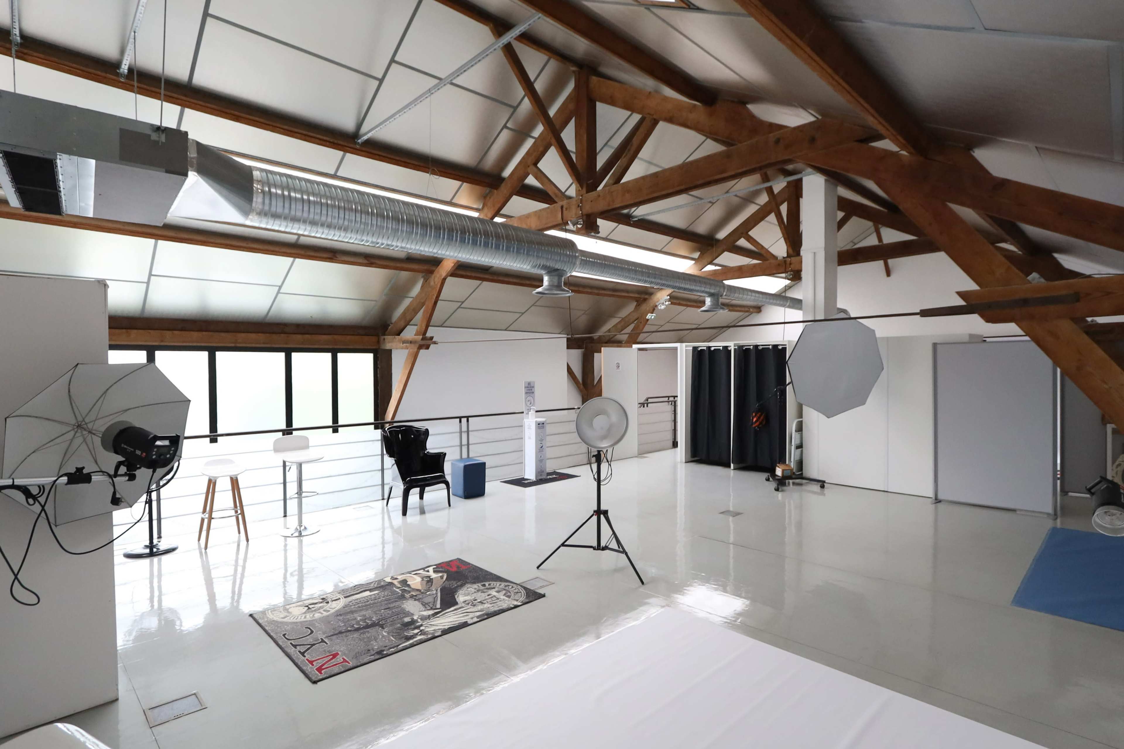 A spacious photography studio with wooden beams, various lighting equipment, and a clean, glossy floor.