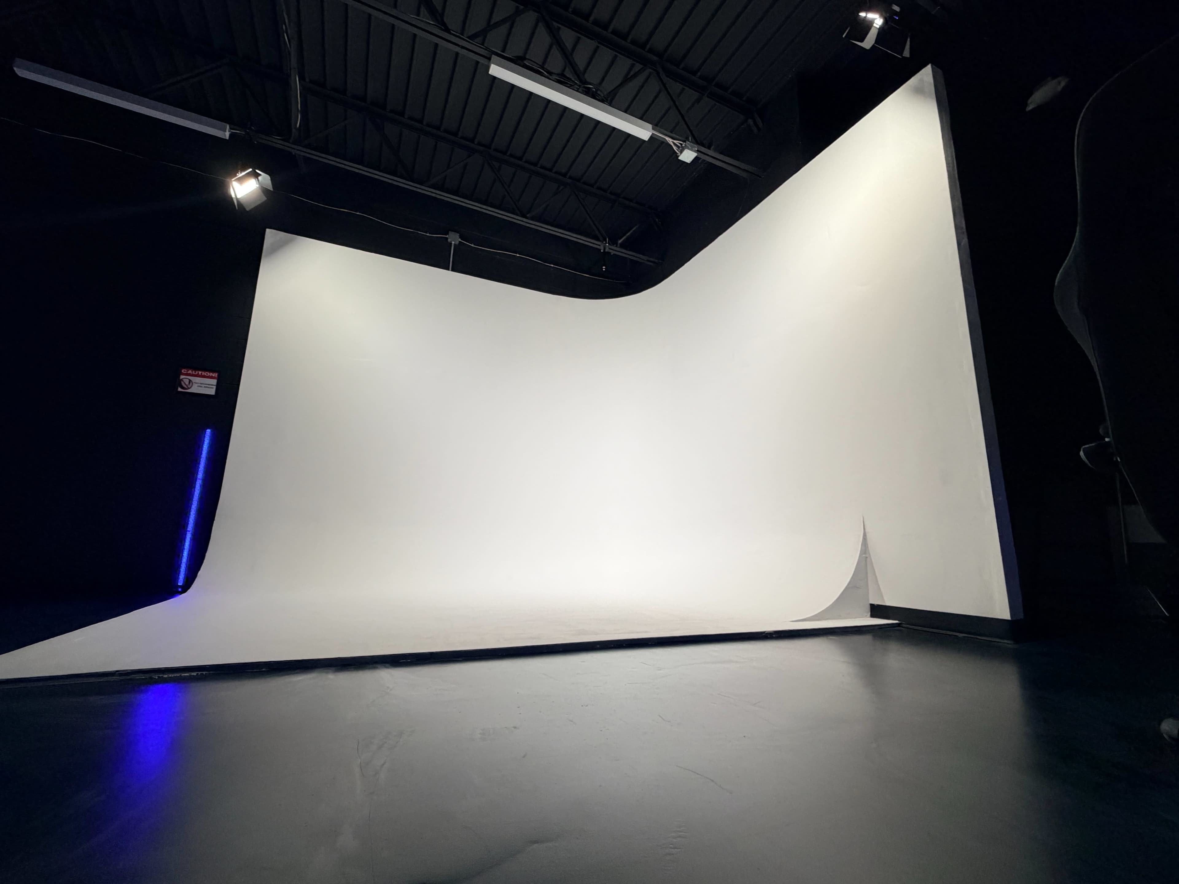 The image shows a spacious, empty studio with a large white curved backdrop and minimal lighting.