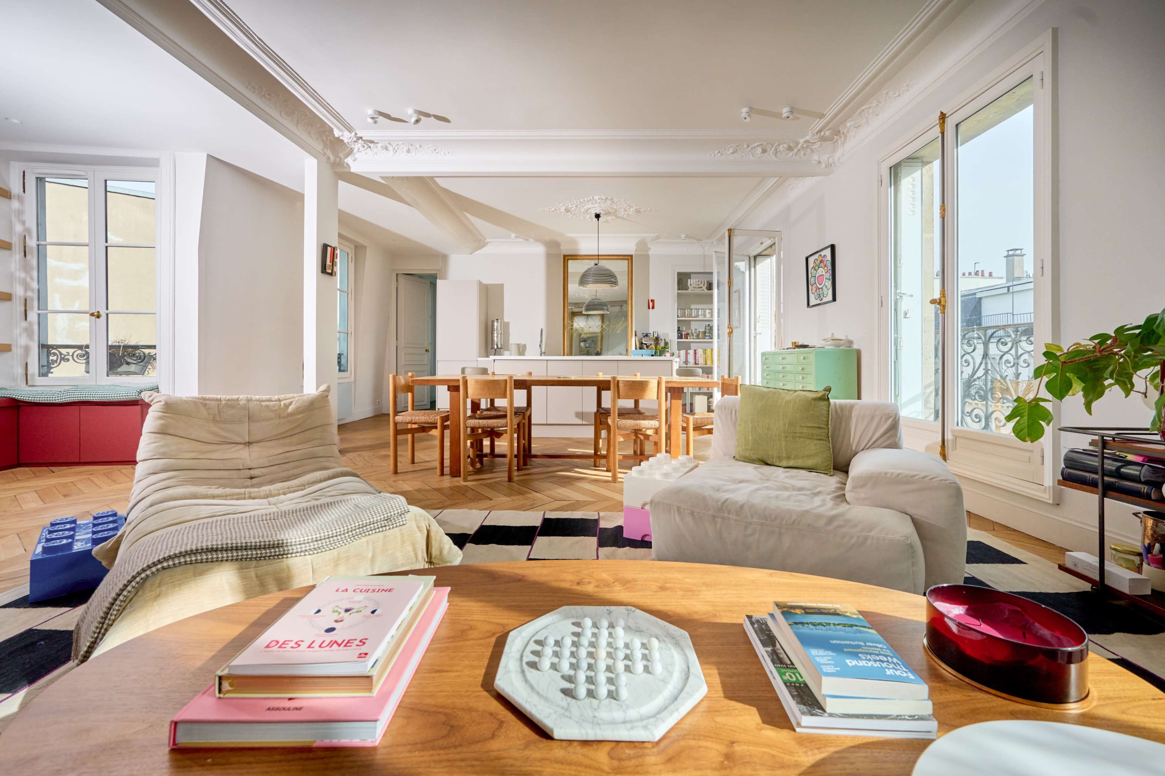 A bright, modern living space features a cozy seating area, a dining table, and a well-lit kitchen with large windows.