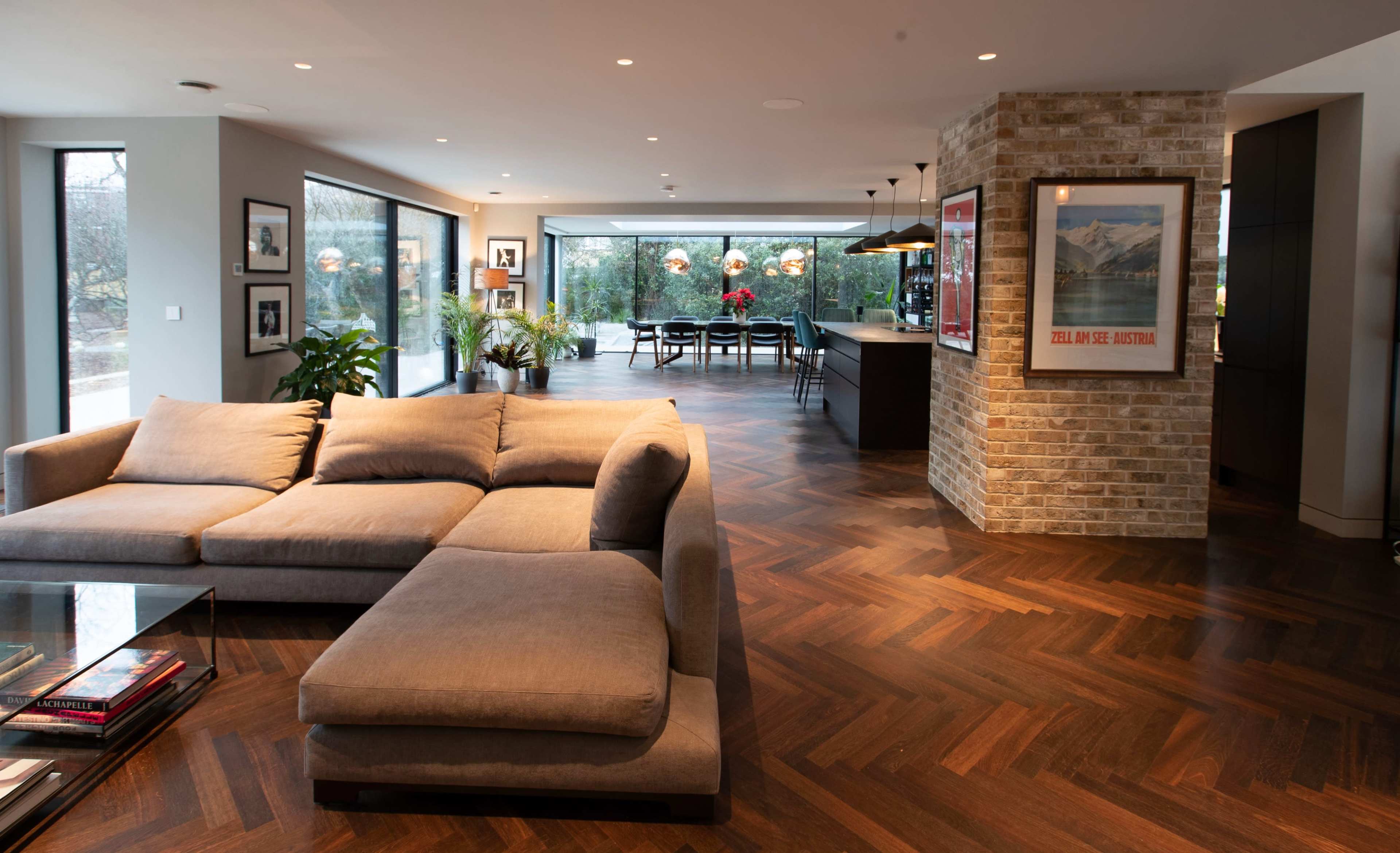 A modern living room with a sectional couch, a brick wall feature, and large windows revealing an outdoor view.