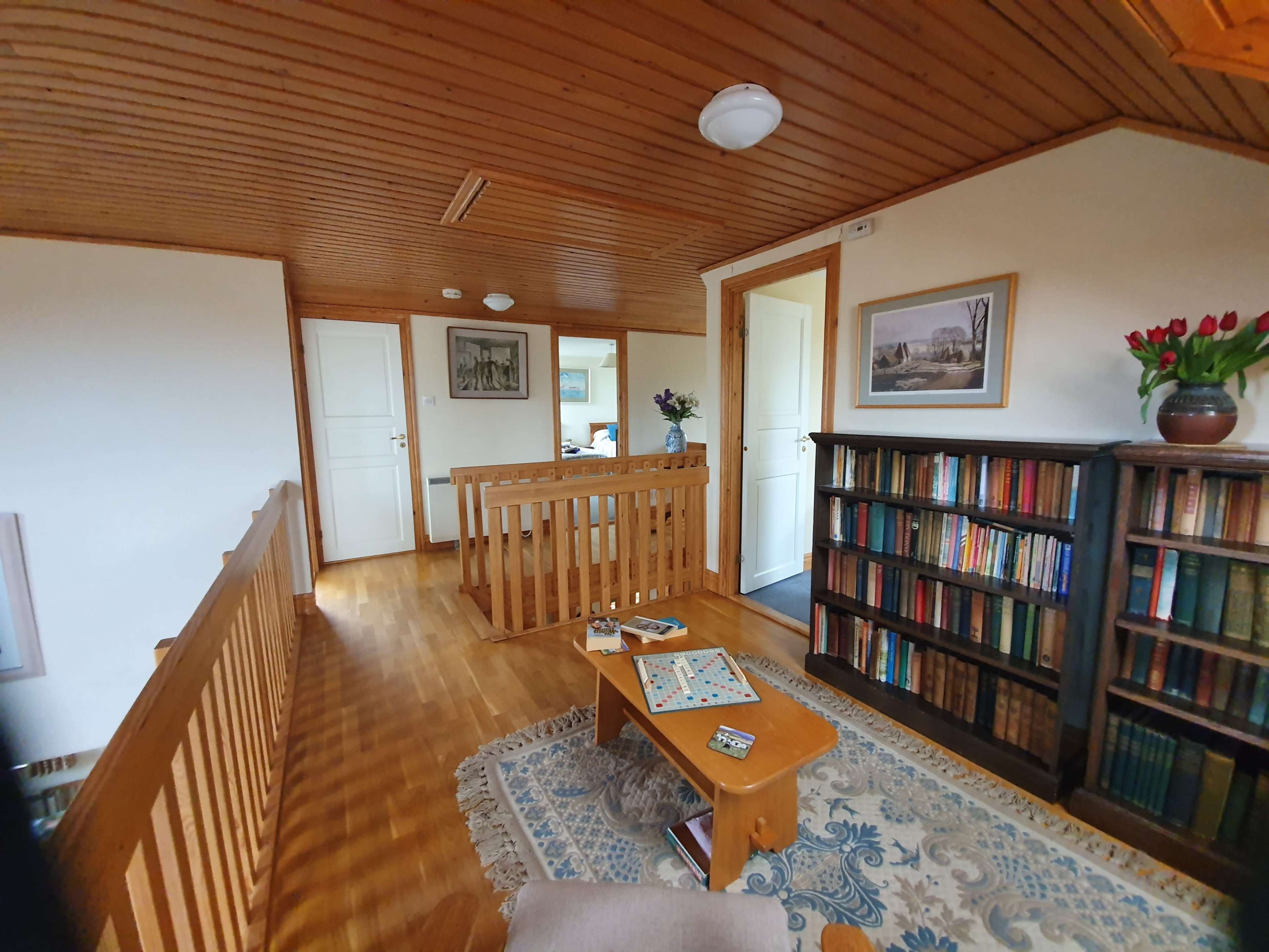 A wooden-floored hallway with a bookshelf, a small table, and doors leading to other rooms.