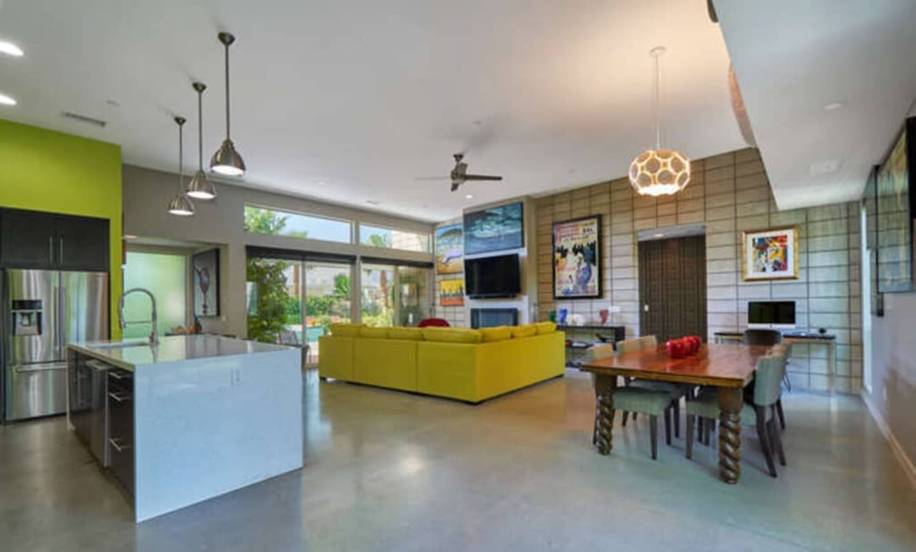 A modern open-concept living space featuring a kitchen island, a dining table, and a seating area with a bright yellow couch.
