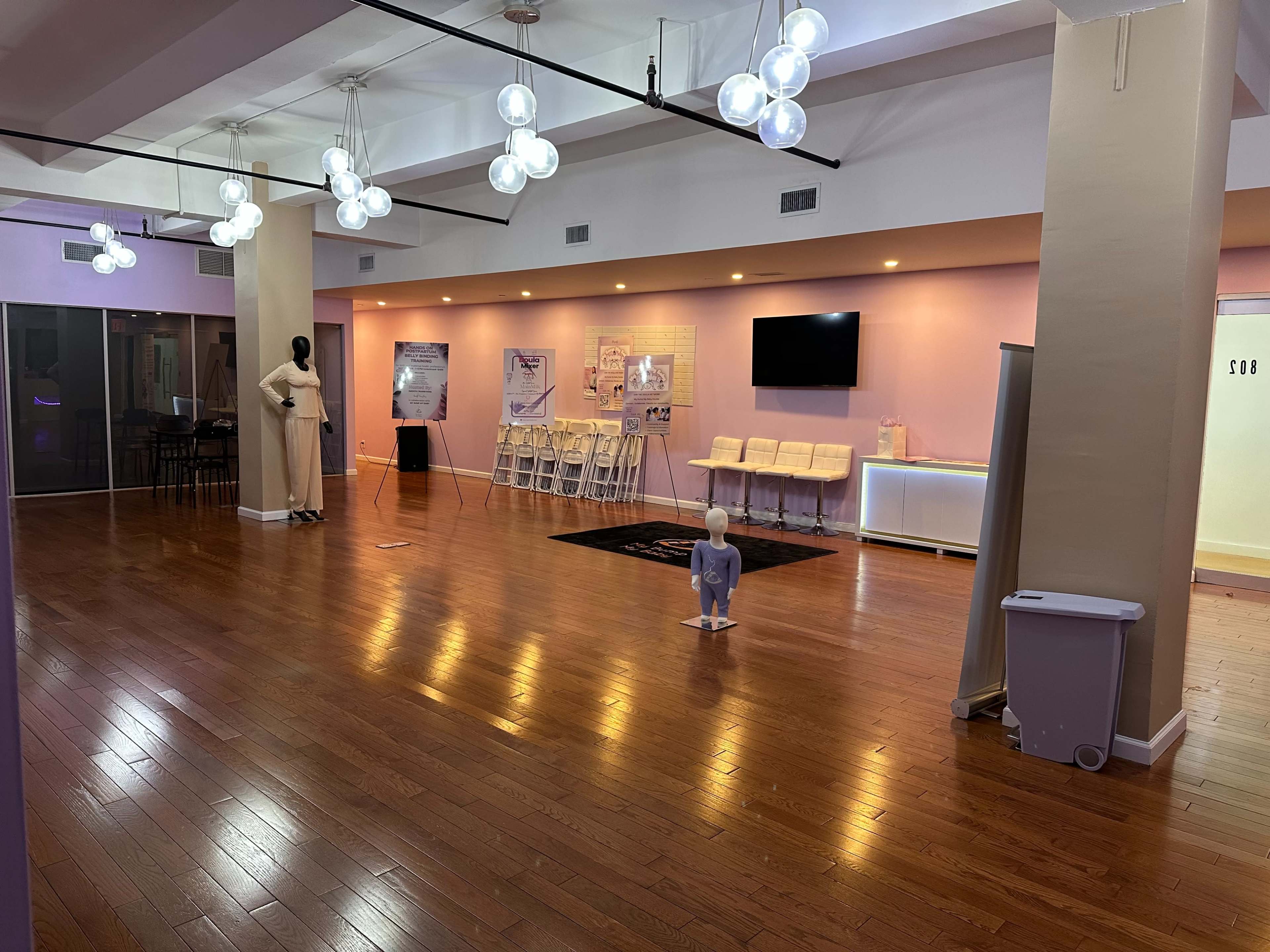 The image shows an empty event space with polished wooden floors, modern light fixtures, and seating arranged against the walls.
