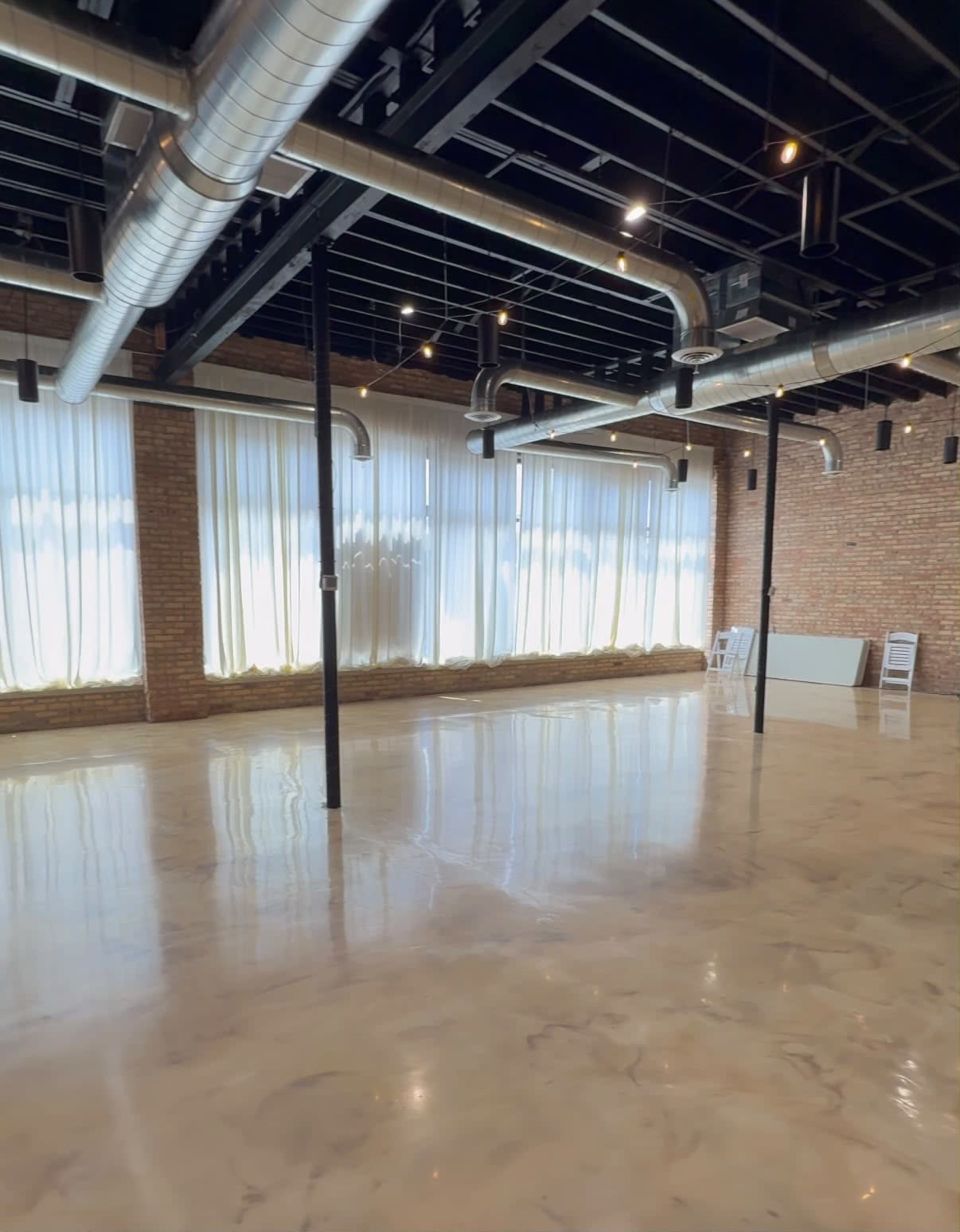 The image shows an empty interior space with polished concrete flooring, exposed ductwork, and large windows covered by sheer curtains.