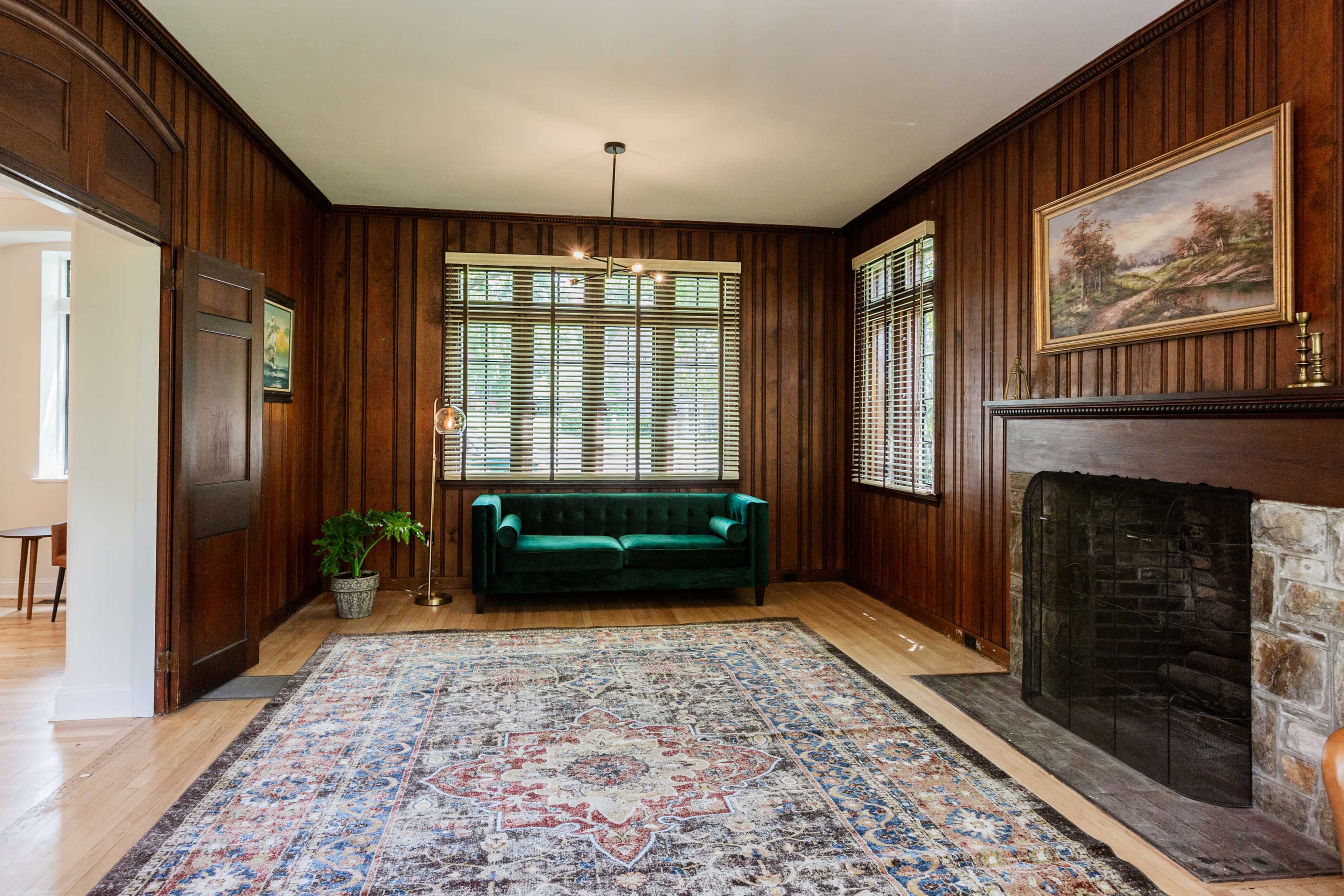 A living room with wooden walls, a green velvet sofa, and a patterned area rug in front of a stone fireplace.