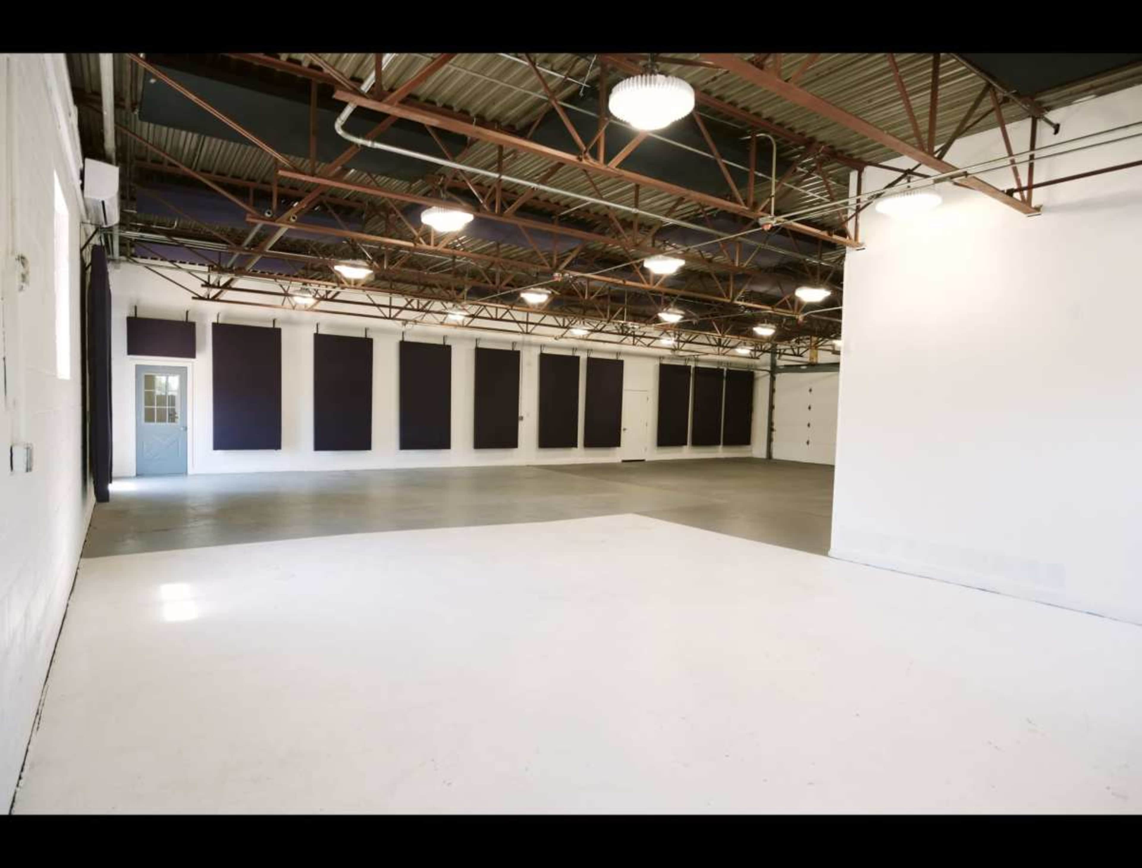 The image shows a spacious, empty warehouse or studio with concrete flooring, high ceilings, and walls equipped with soundproof panels.