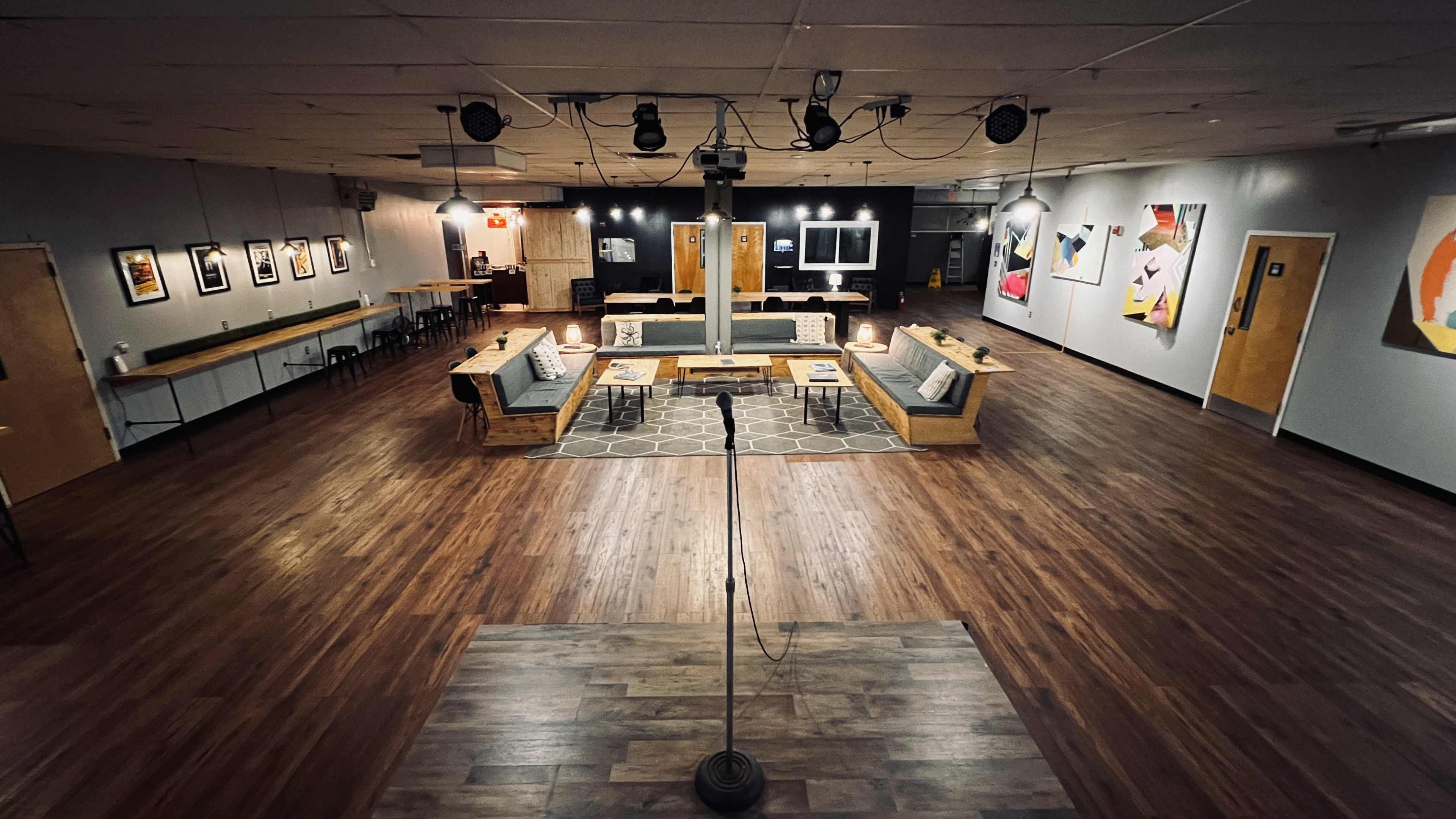 A spacious indoor lounge area with wooden flooring, featuring several seating arrangements, artwork on the walls, and a central performance space.