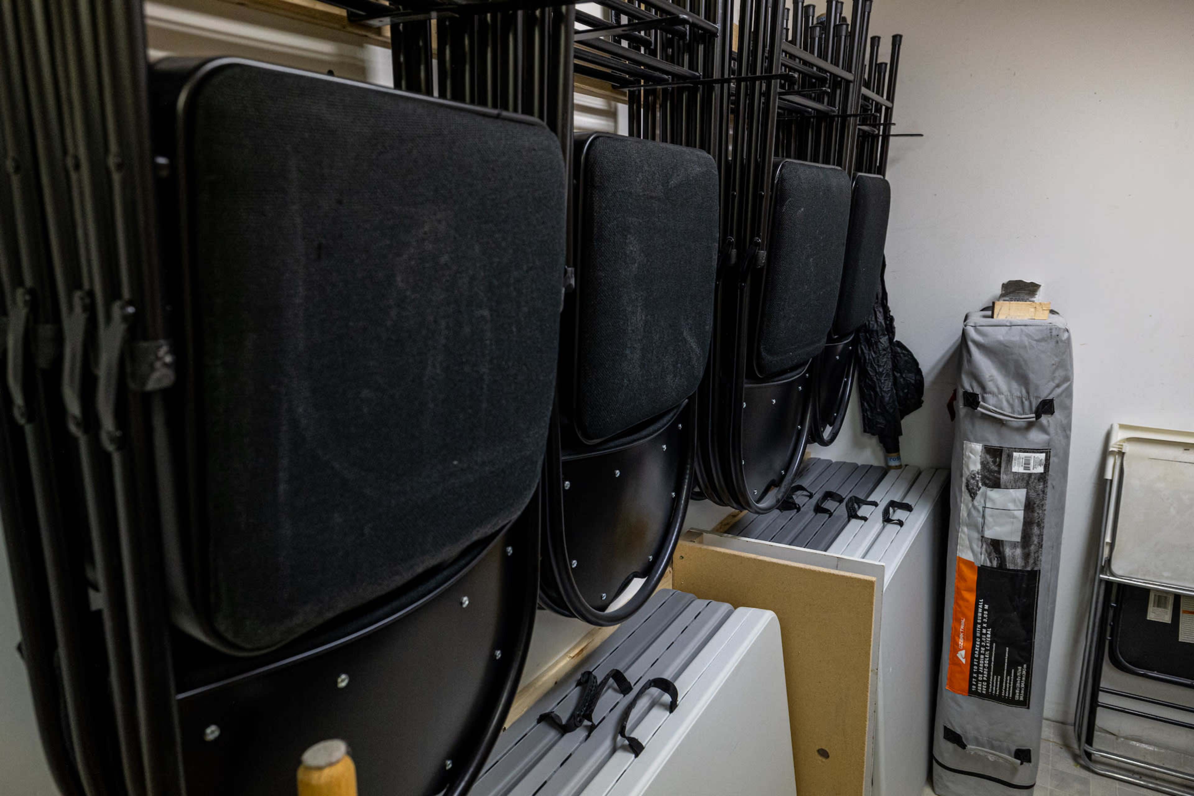 Several stacked black folding chairs next to a rolled-up tent and various items stored in a small room.
