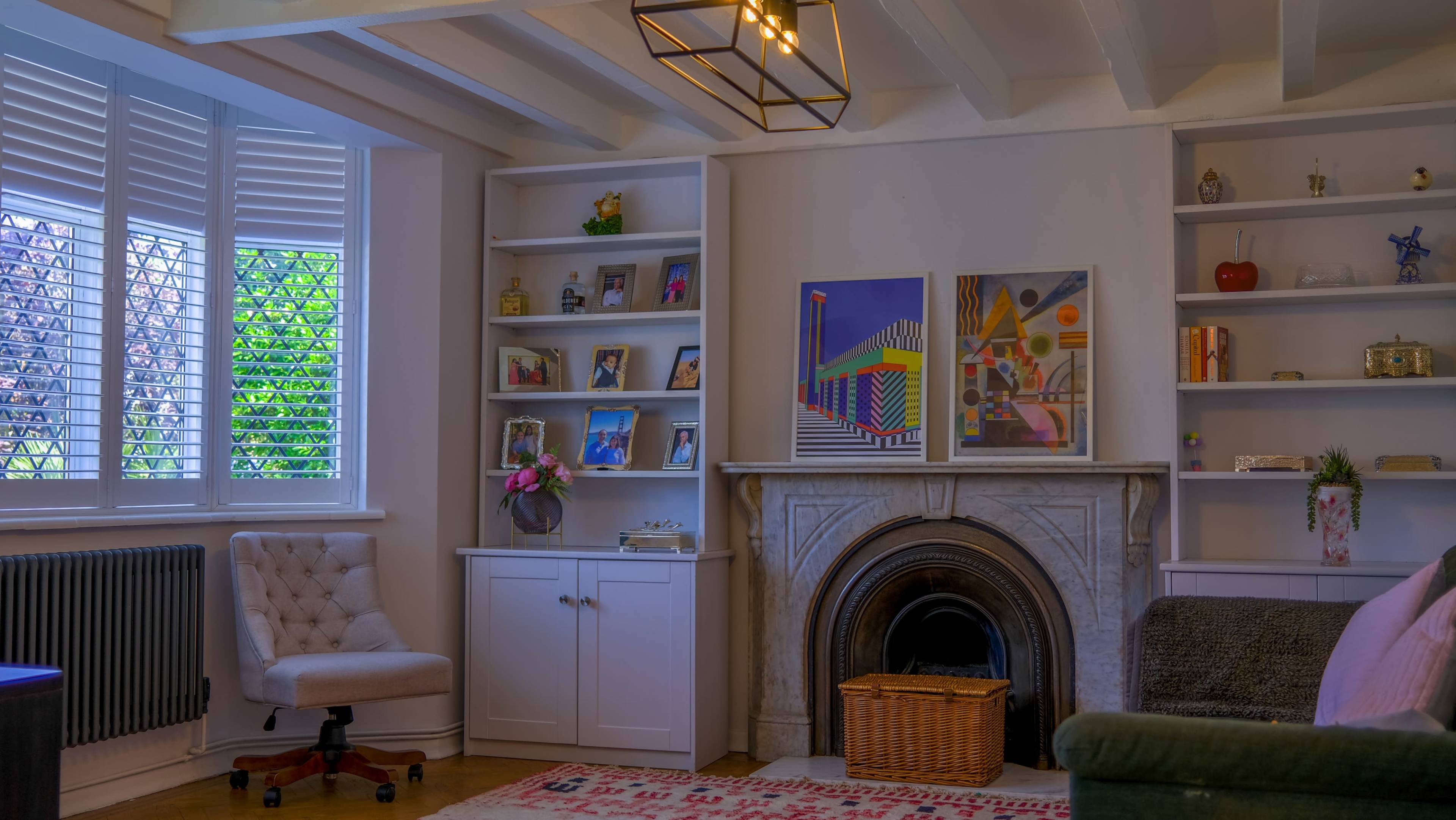 A cozy living room featuring a marble fireplace, white shelves filled with decorative items and pictures, a green sofa, and a light-colored armchair.