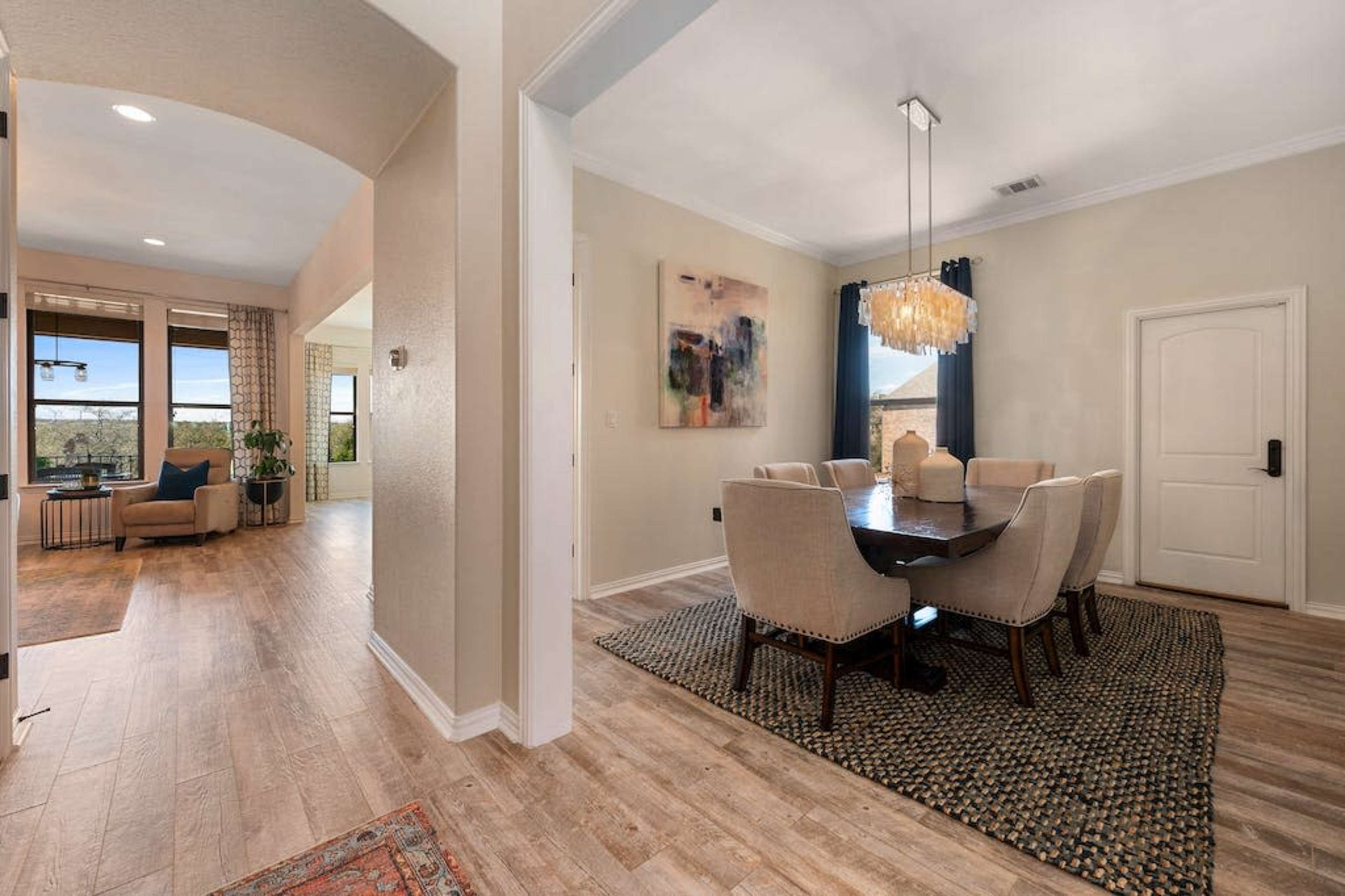 A spacious dining area features a dark wooden table surrounded by upholstered chairs, leading to an open living space with large windows.