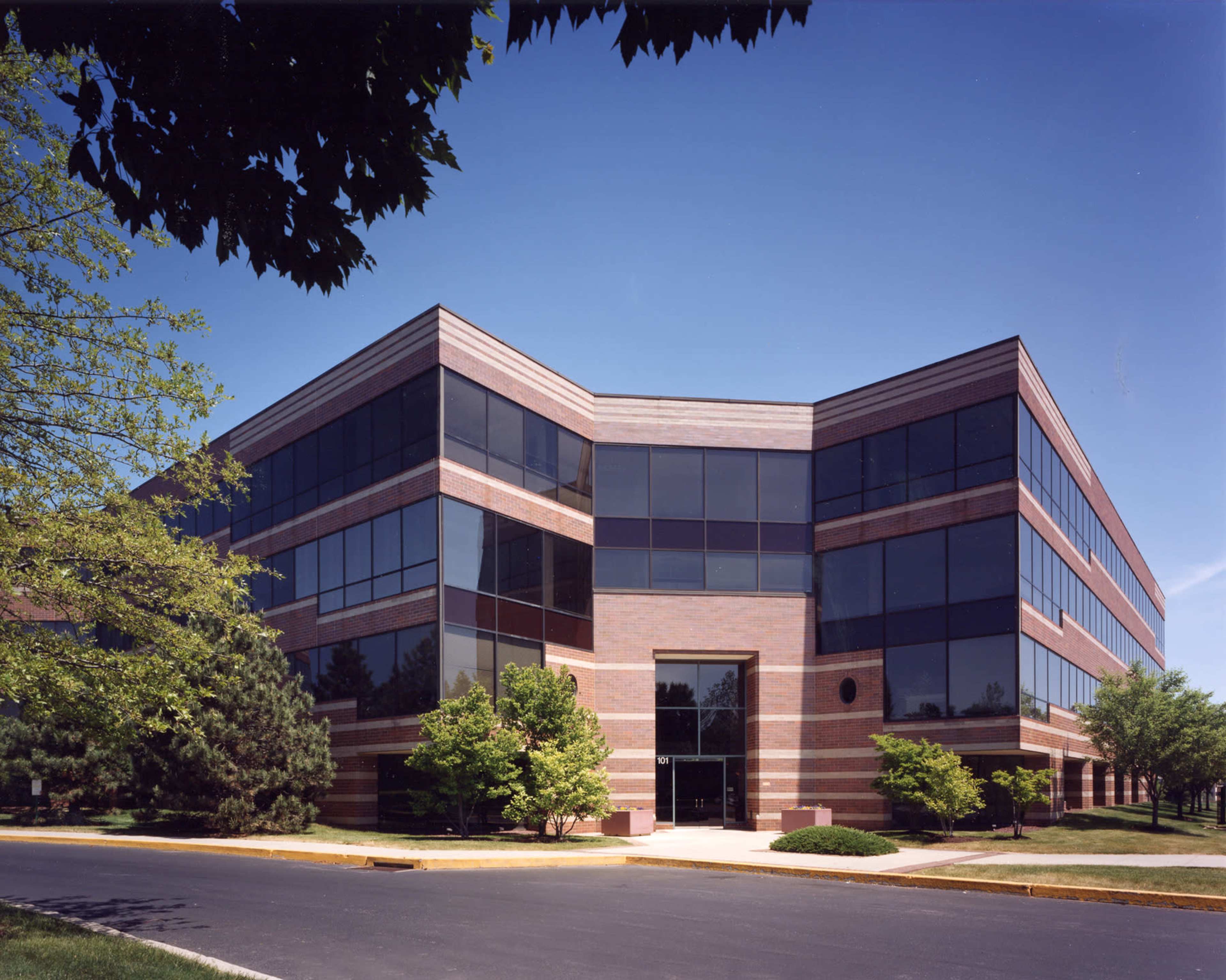 A modern brick office building with large windows is surrounded by landscaped greenery.
