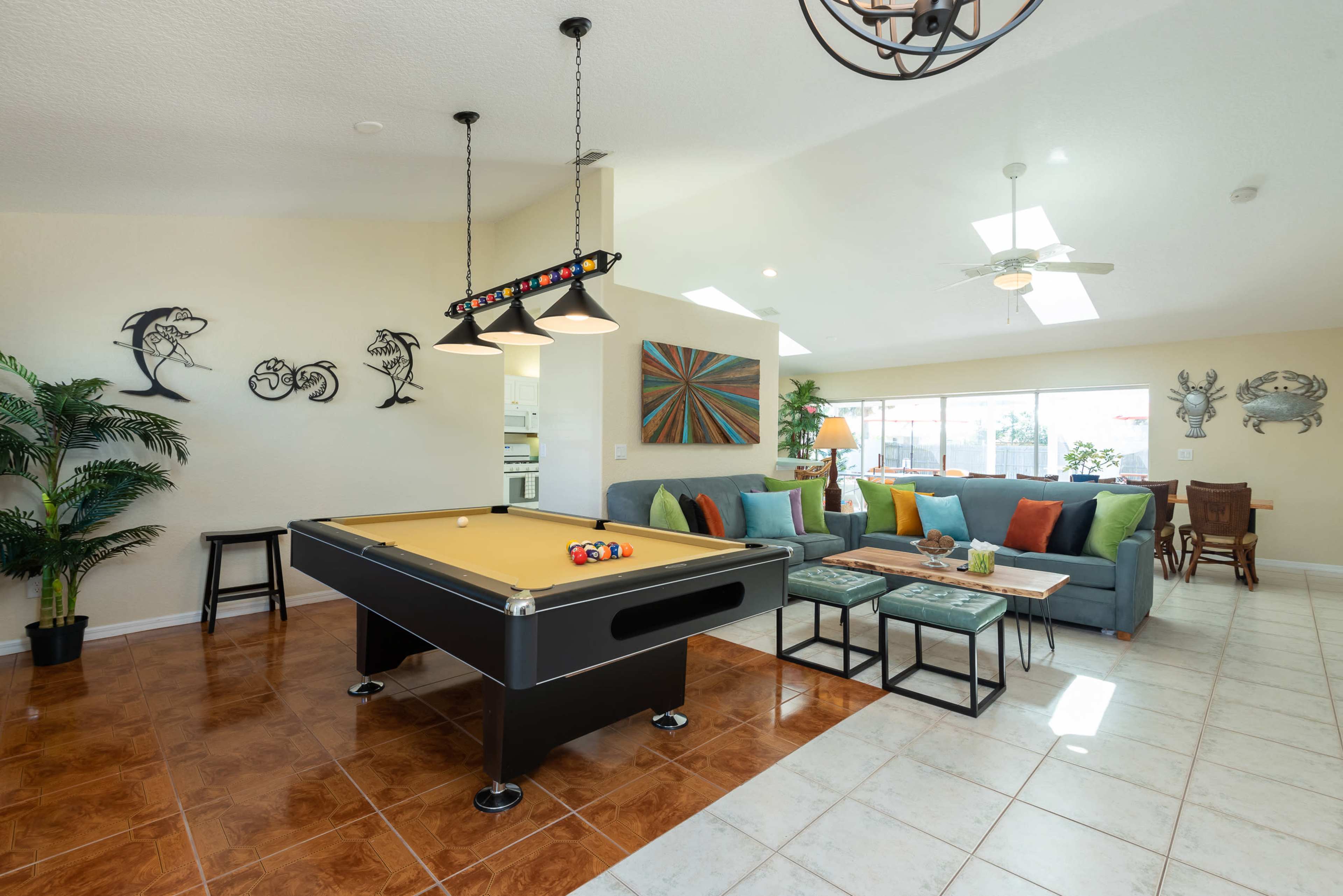 A spacious living area featuring a billiard table, a large sectional sofa with colorful cushions, and various decorative elements on the walls.