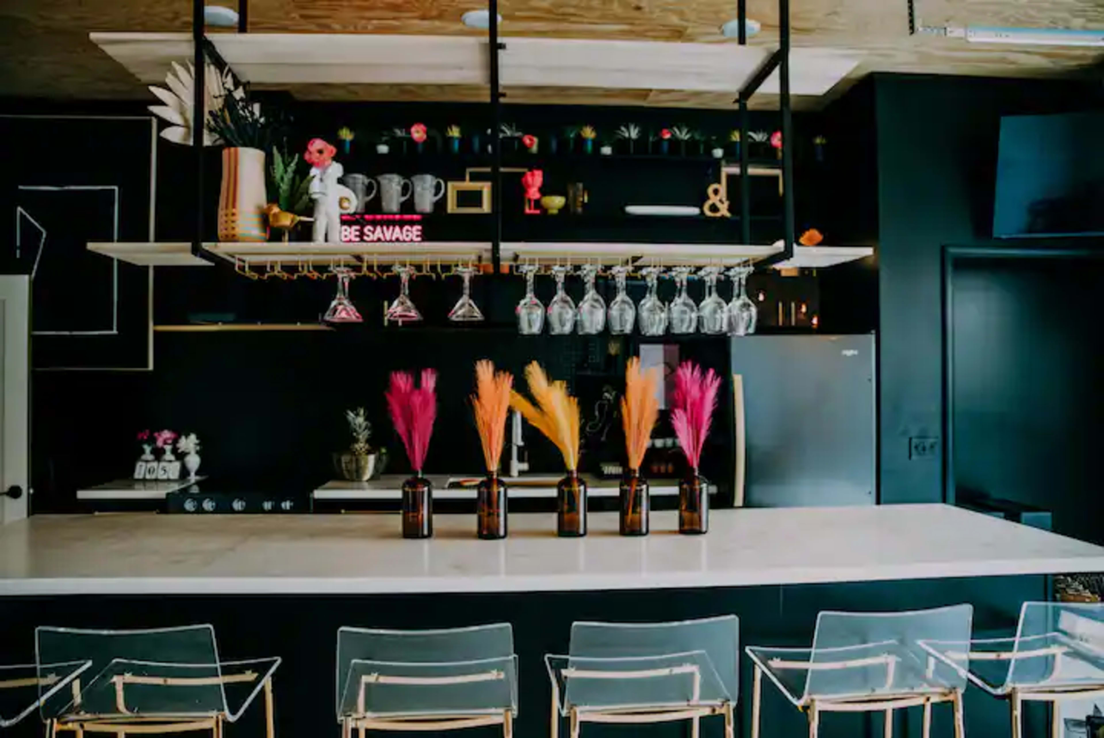 A modern bar with a black wall, a white countertop, and decorative plants in glass vases on display.