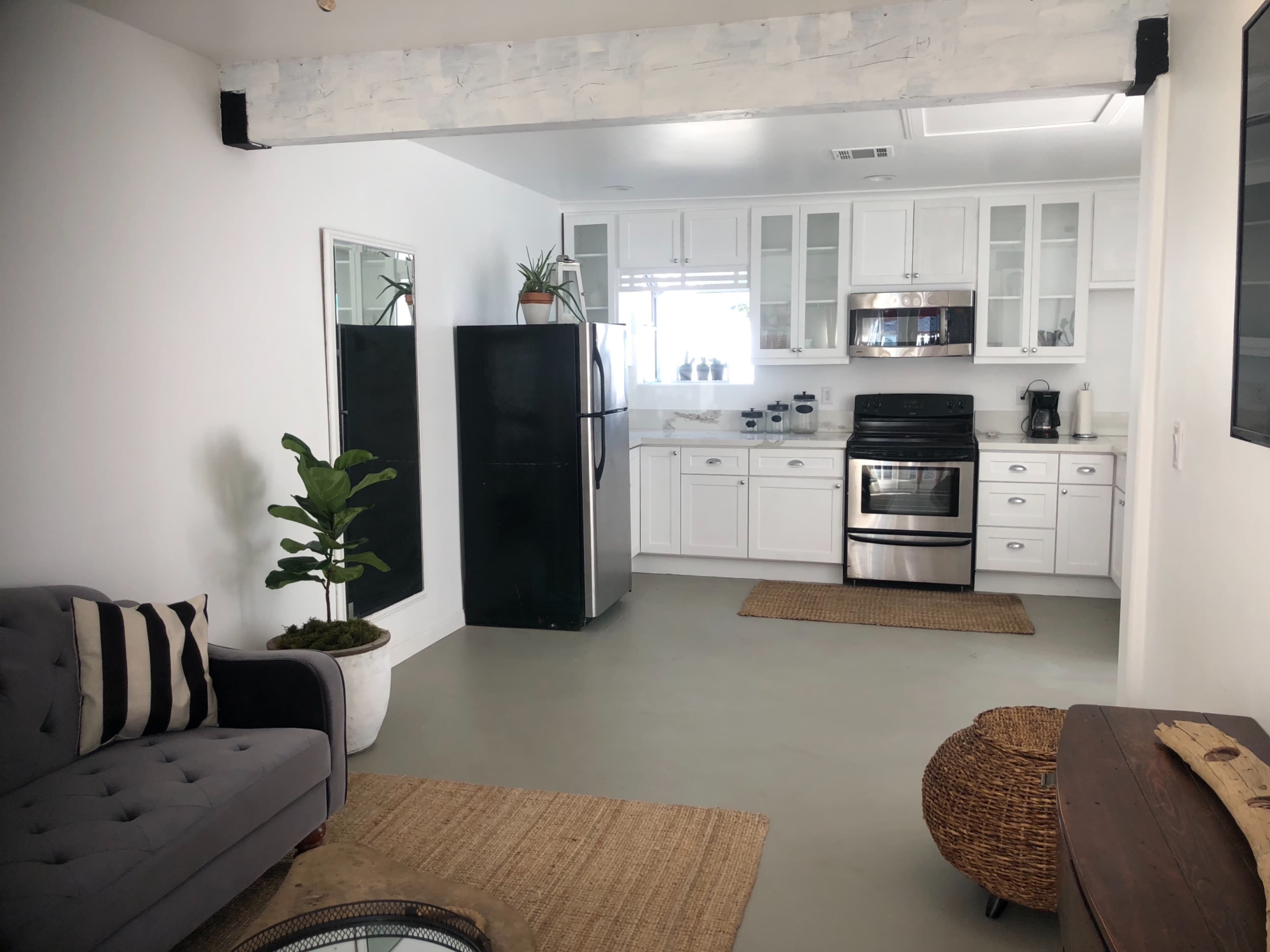 A modern kitchen and living area featuring a black refrigerator, stainless steel stove, white cabinetry, and a gray sofa.