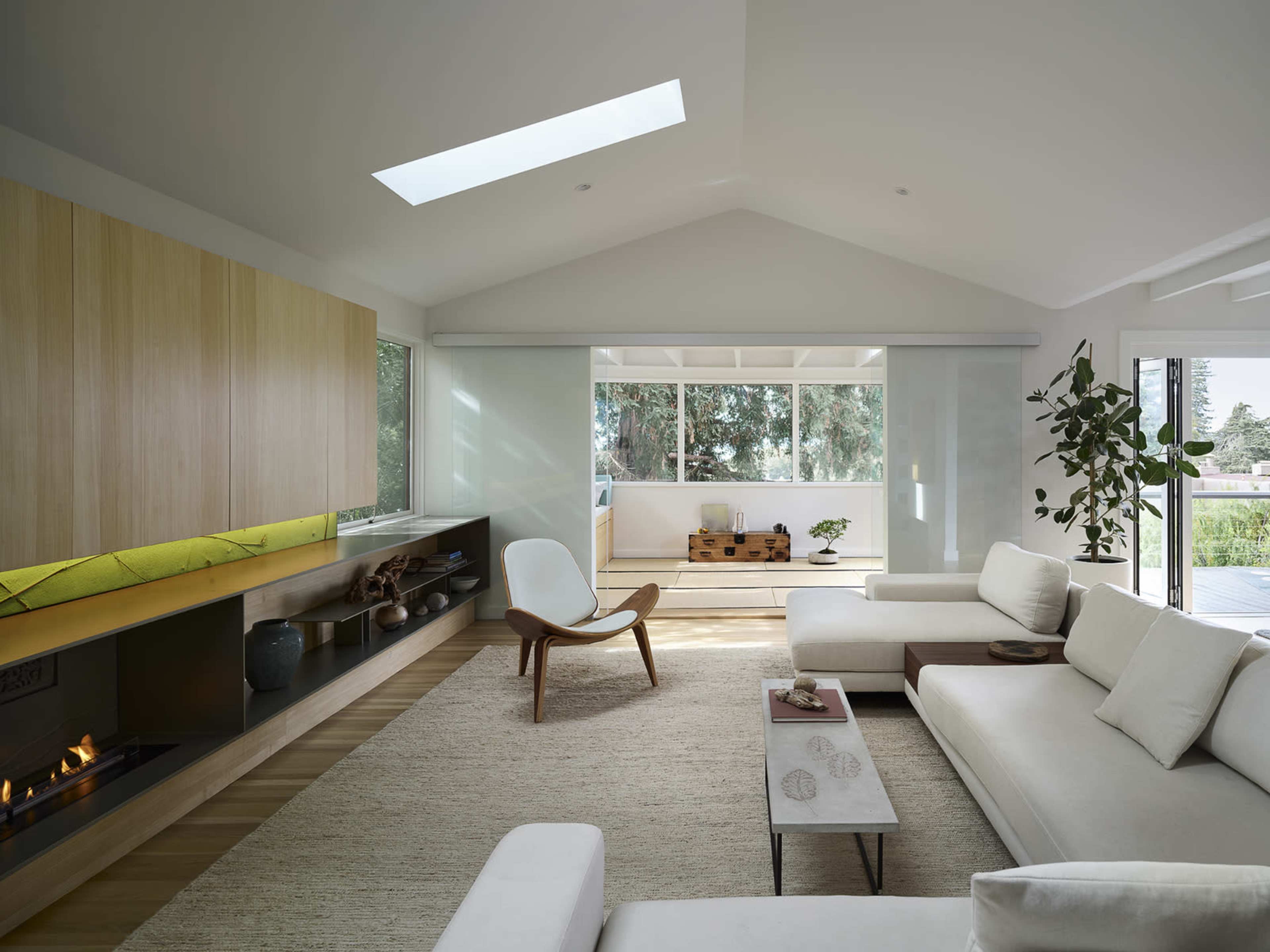 A modern living room features a white sectional sofa, a minimalist coffee table, and large windows illuminating the space with natural light.