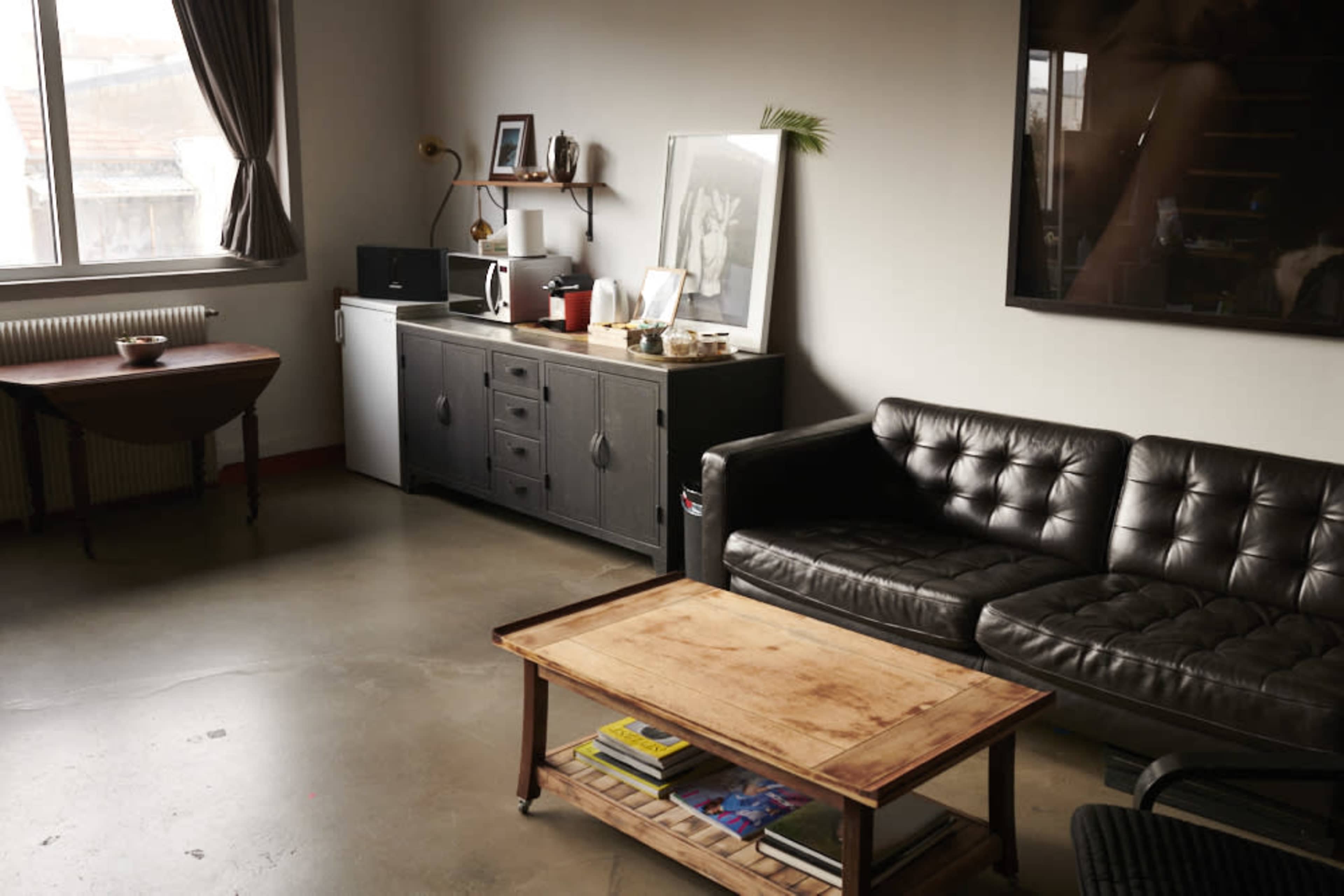 A modern living room with a black leather sofa, a wooden coffee table, a sideboard, and various decorative items on the walls and surfaces.