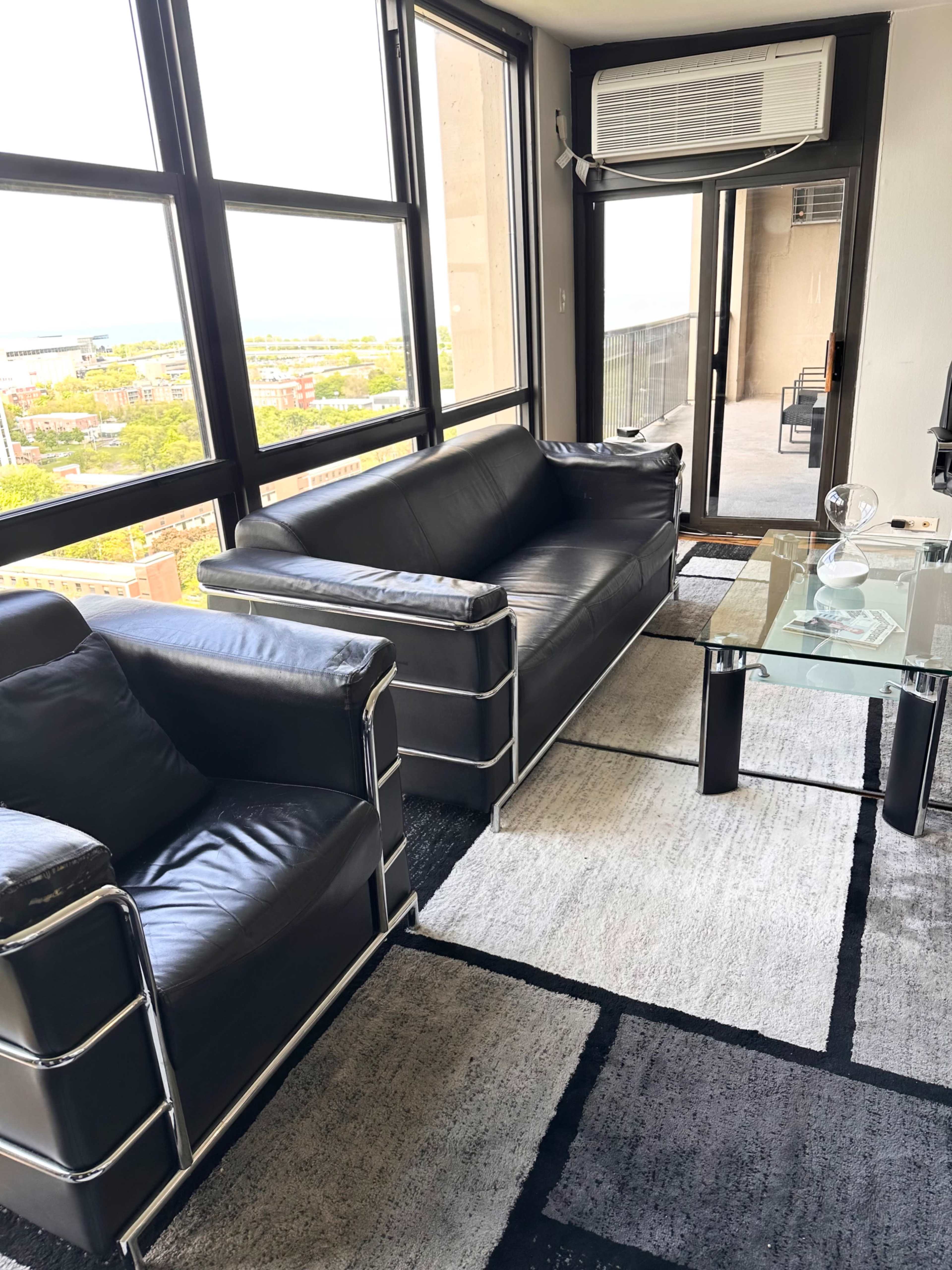 The image shows a modern living room with black leather furniture, including a sofa and an armchair, alongside a glass coffee table on a patterned rug.