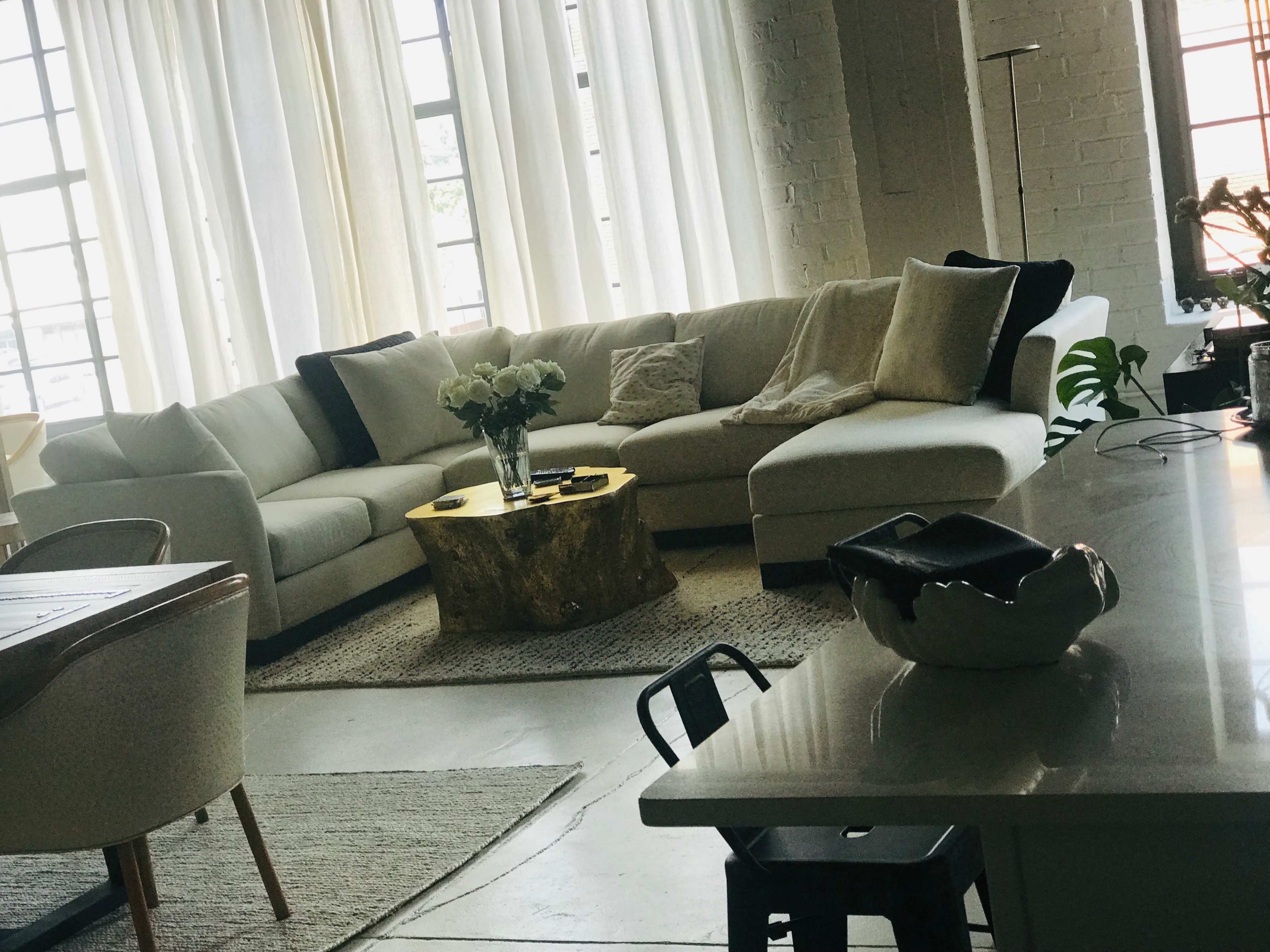 A spacious living area features a large sectional sofa, a round gold coffee table, and a dining table with minimalist decor.