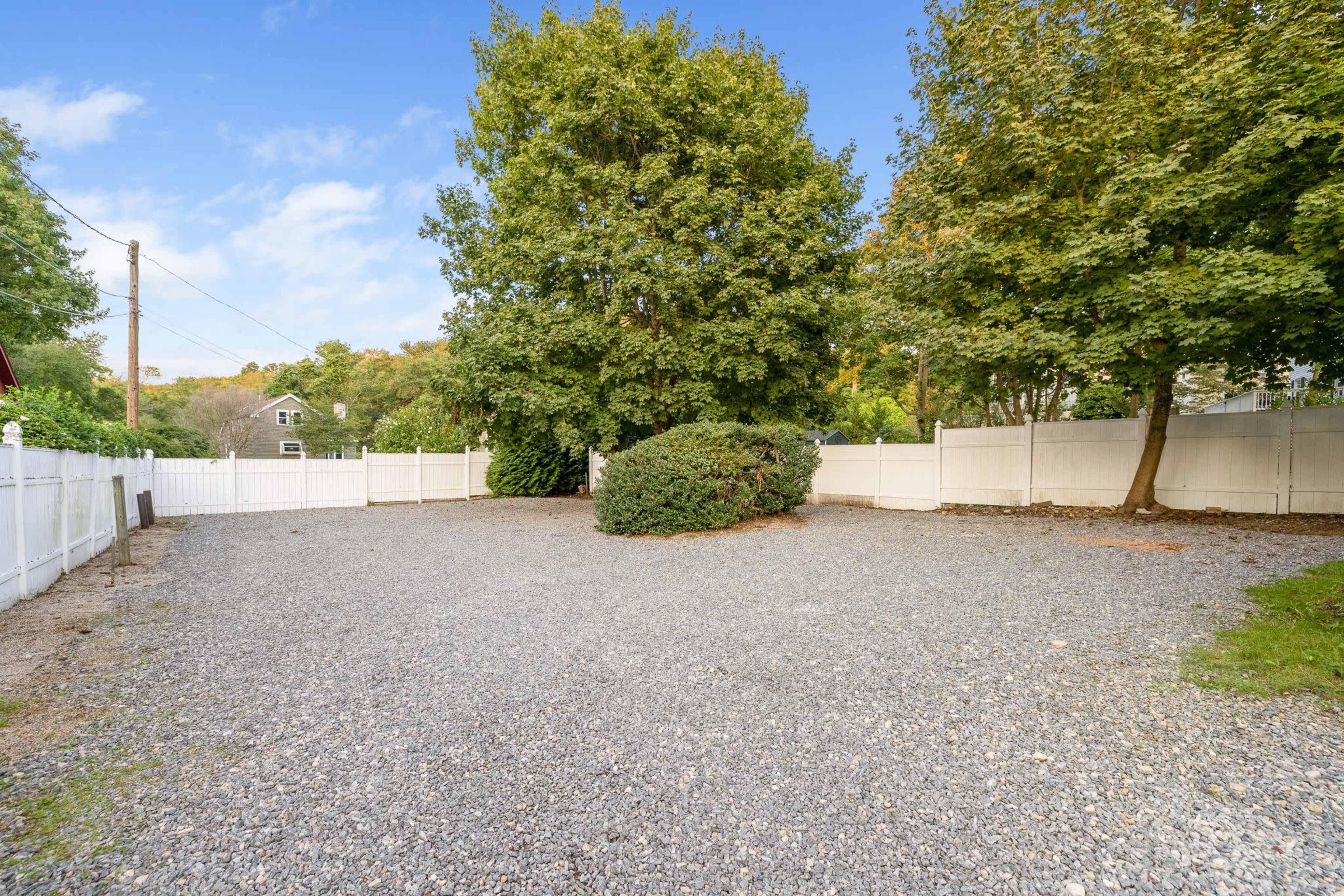 A gravel area is enclosed by a white fence and features two trees in the center.