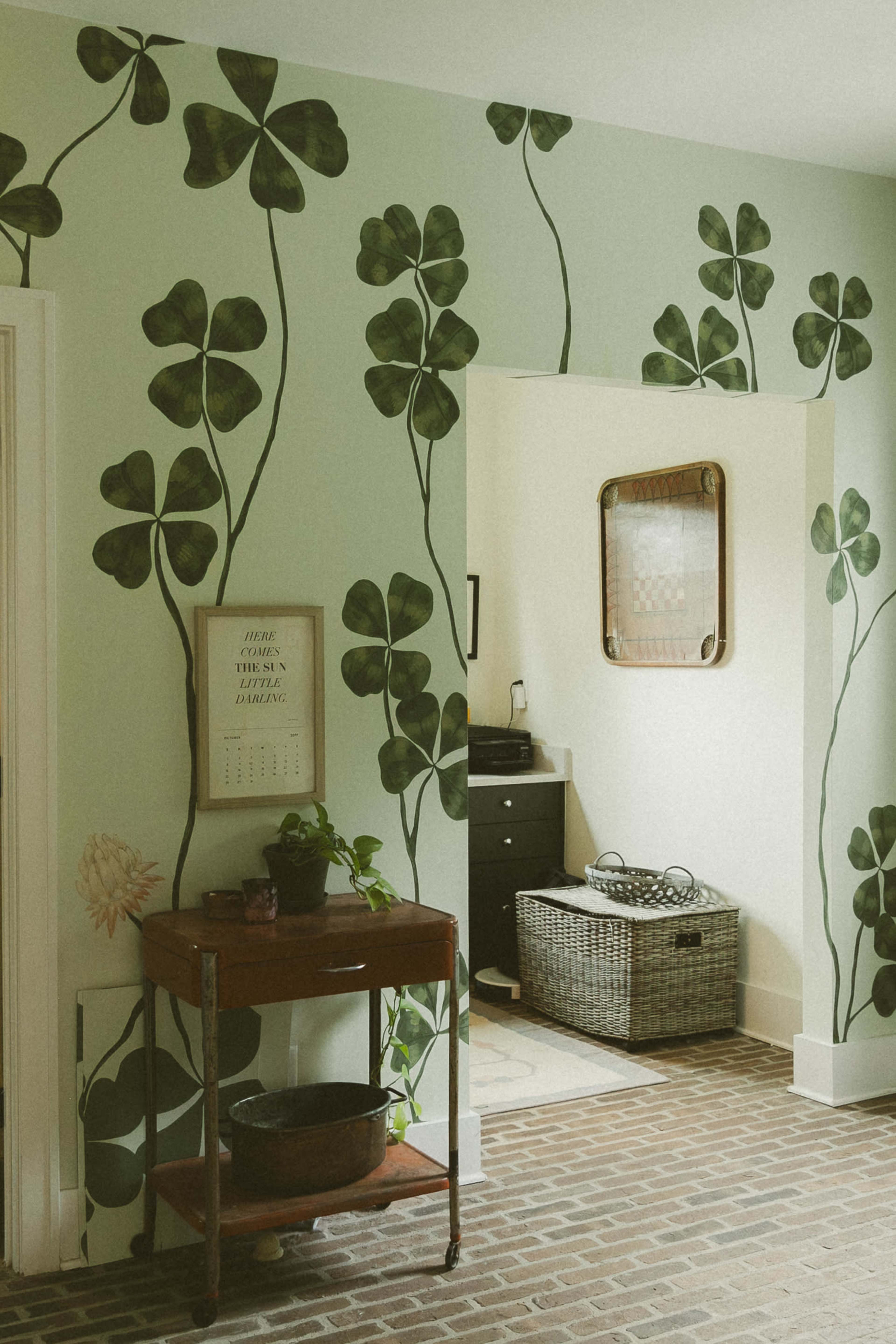 The image features a wall adorned with green leaf patterns, leading to an open doorway that reveals a bathroom area.