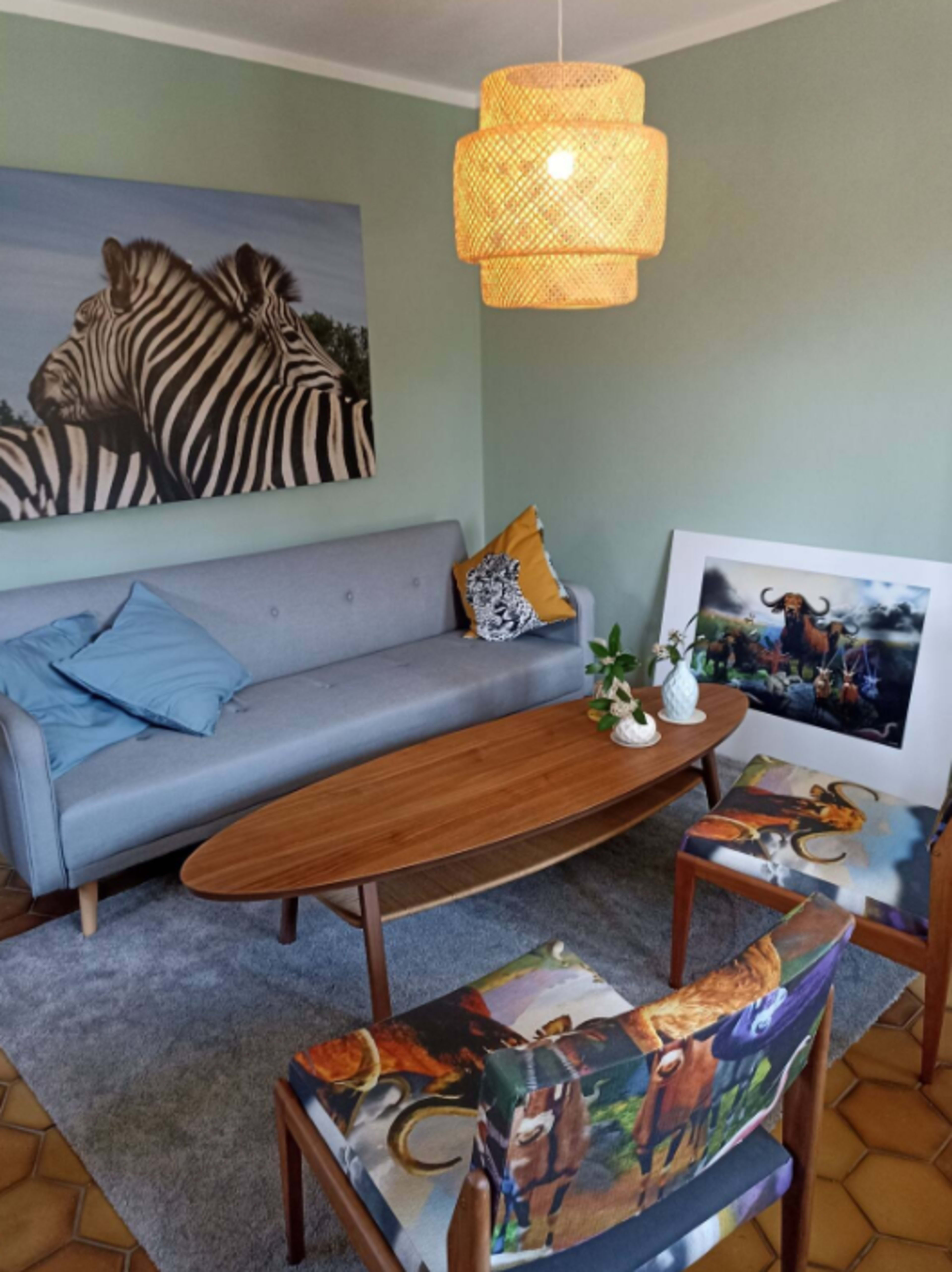 A modern living room features a gray sofa with blue pillows, an oval wooden coffee table, and chairs adorned with animal-themed upholstery, all centered under a woven pendant light.