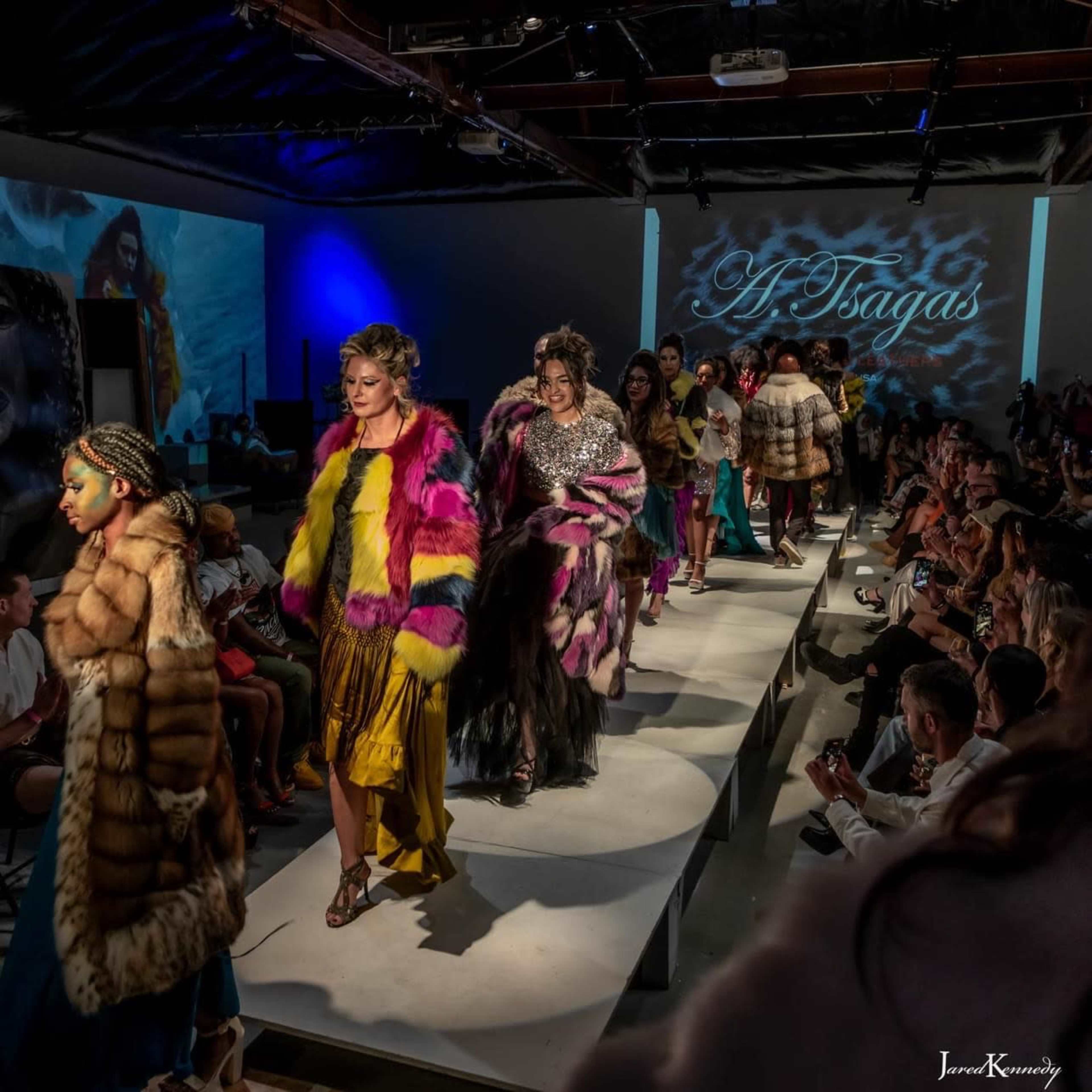 Models walk down a runway showcasing a variety of colorful fur coats and fashionable attire during a fashion show.
