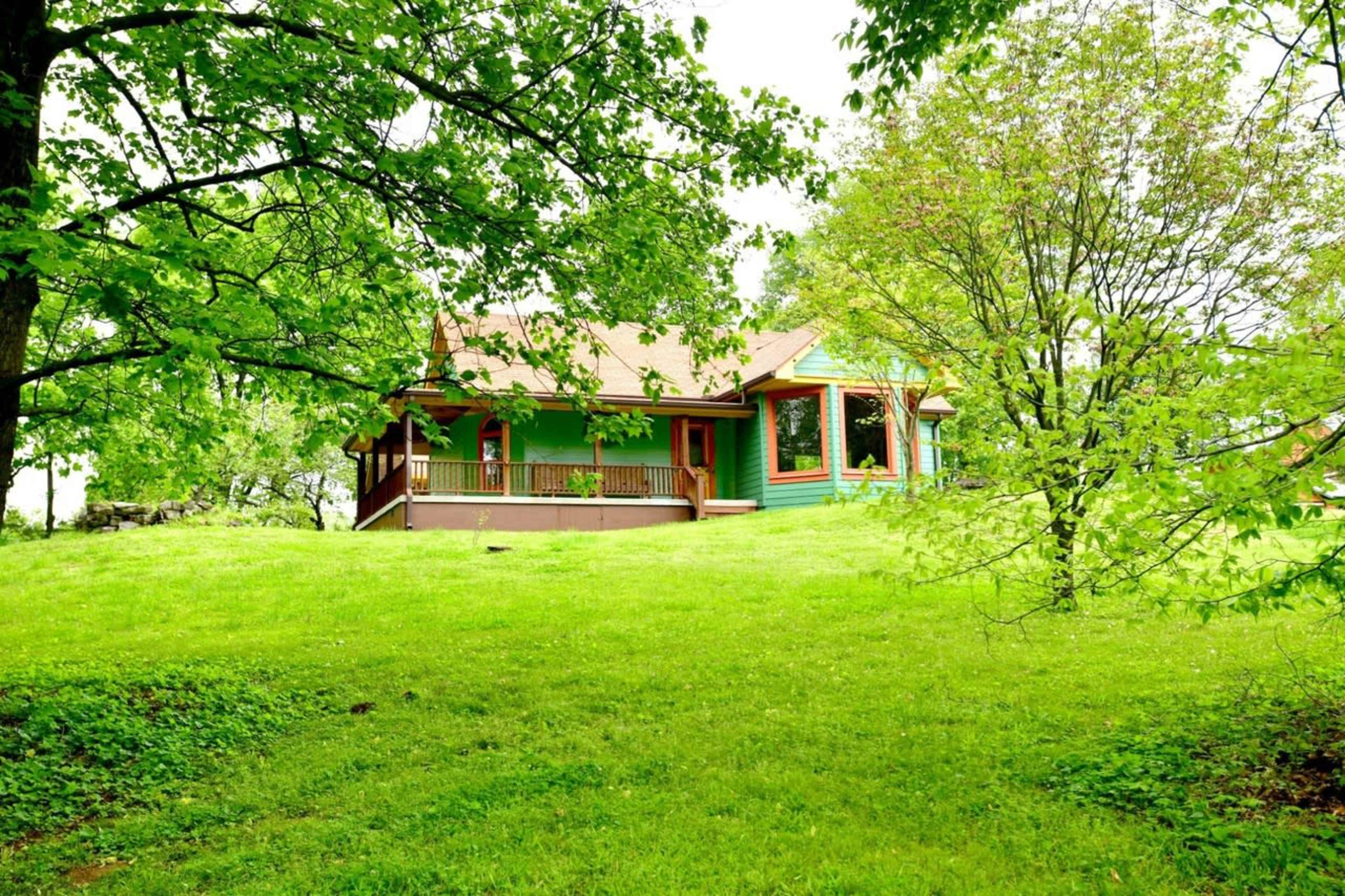 A green house with a wooden porch is surrounded by lush greenery and trees.