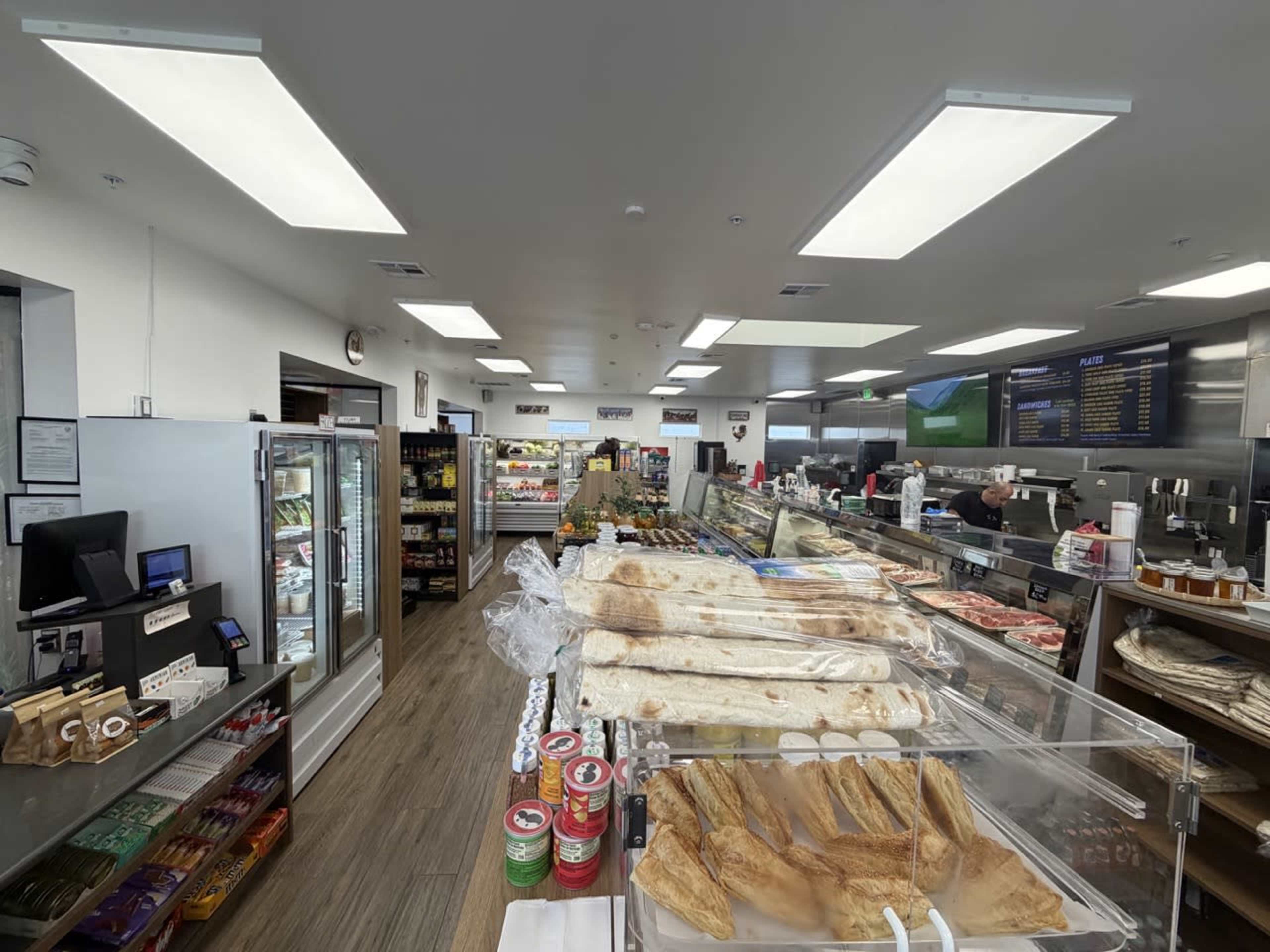 The image shows the interior of a grocery store with display cases filled with various food items, a checkout area, and shelves stocked with products.