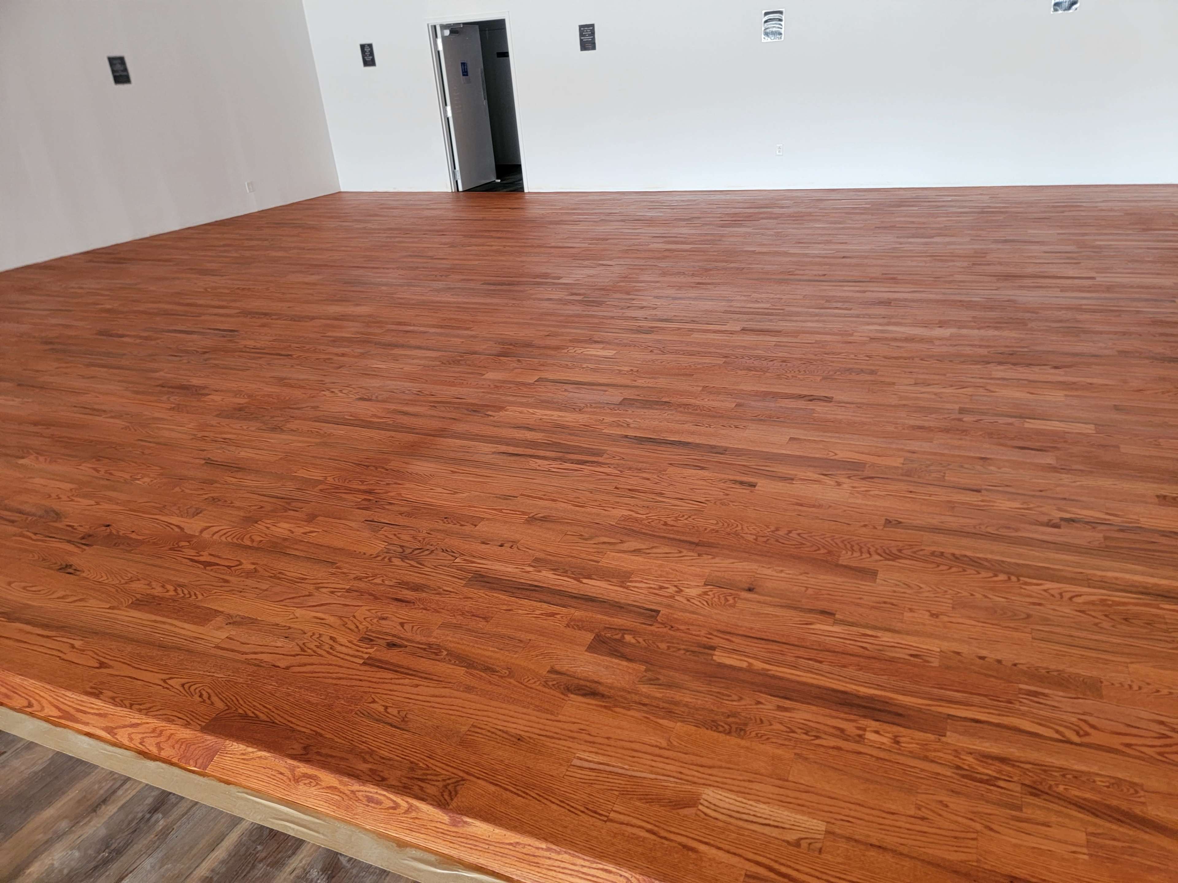A spacious room with a polished wooden floor and plain white walls.