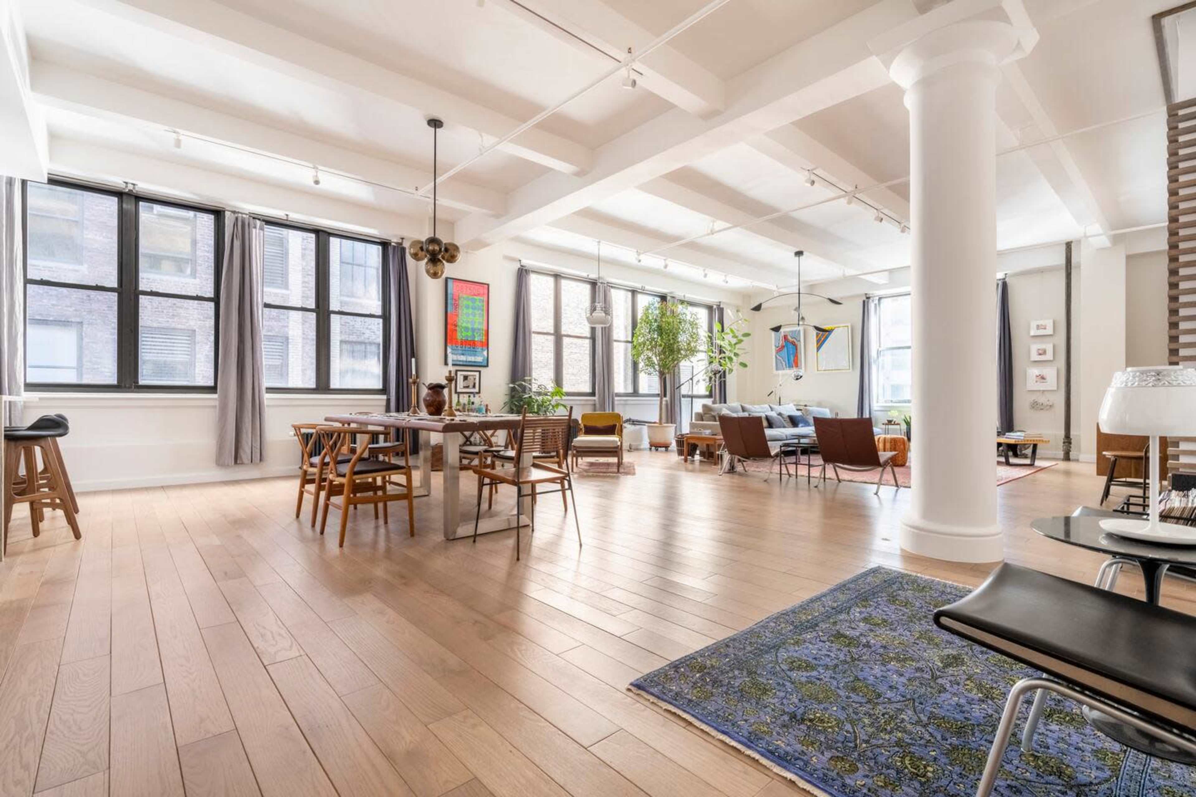 A spacious, modern loft features a mix of dining and living areas with large windows and wooden floors.