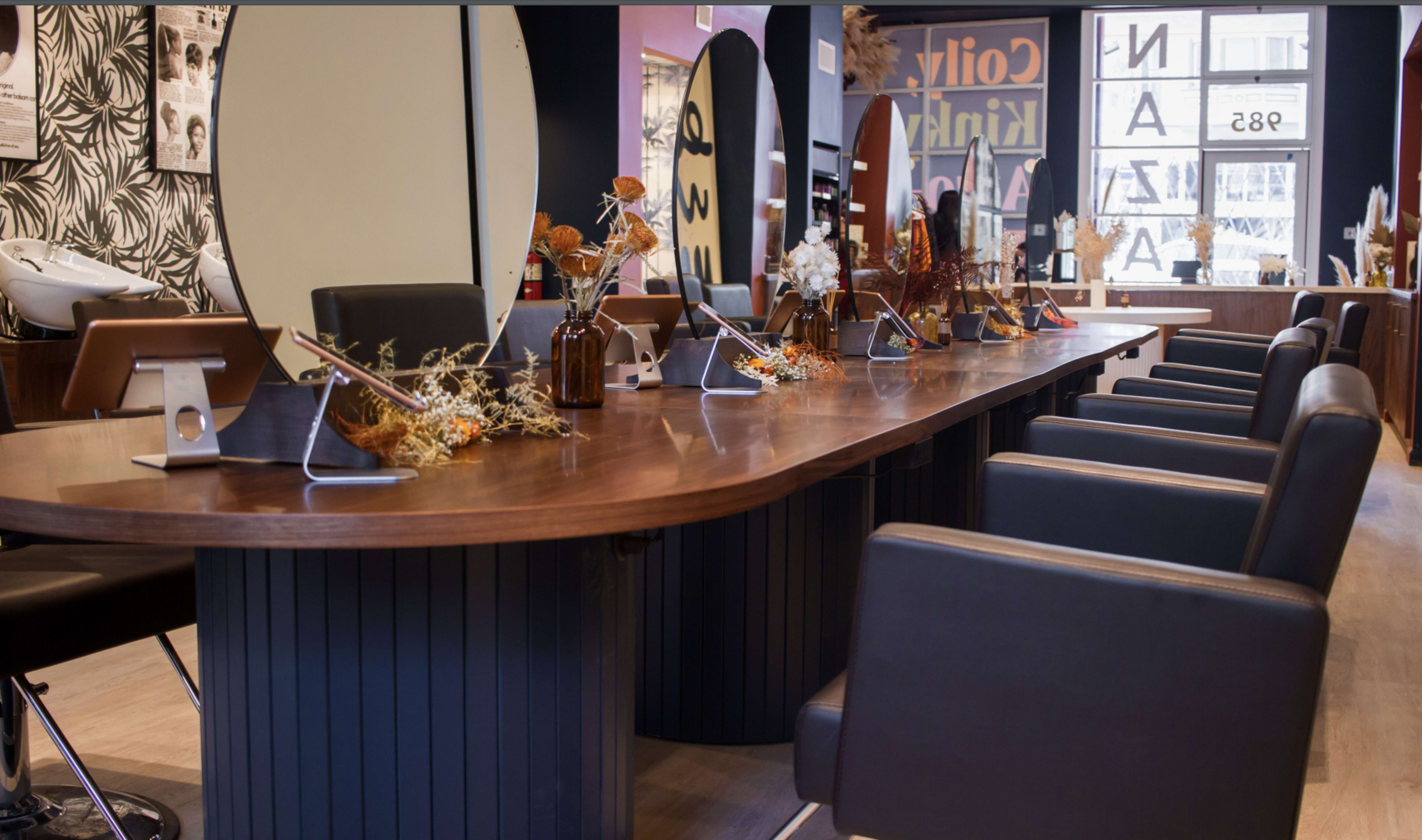 A modern hair salon with a long wooden styling table, equipped with mirrors and chairs arranged in a row.