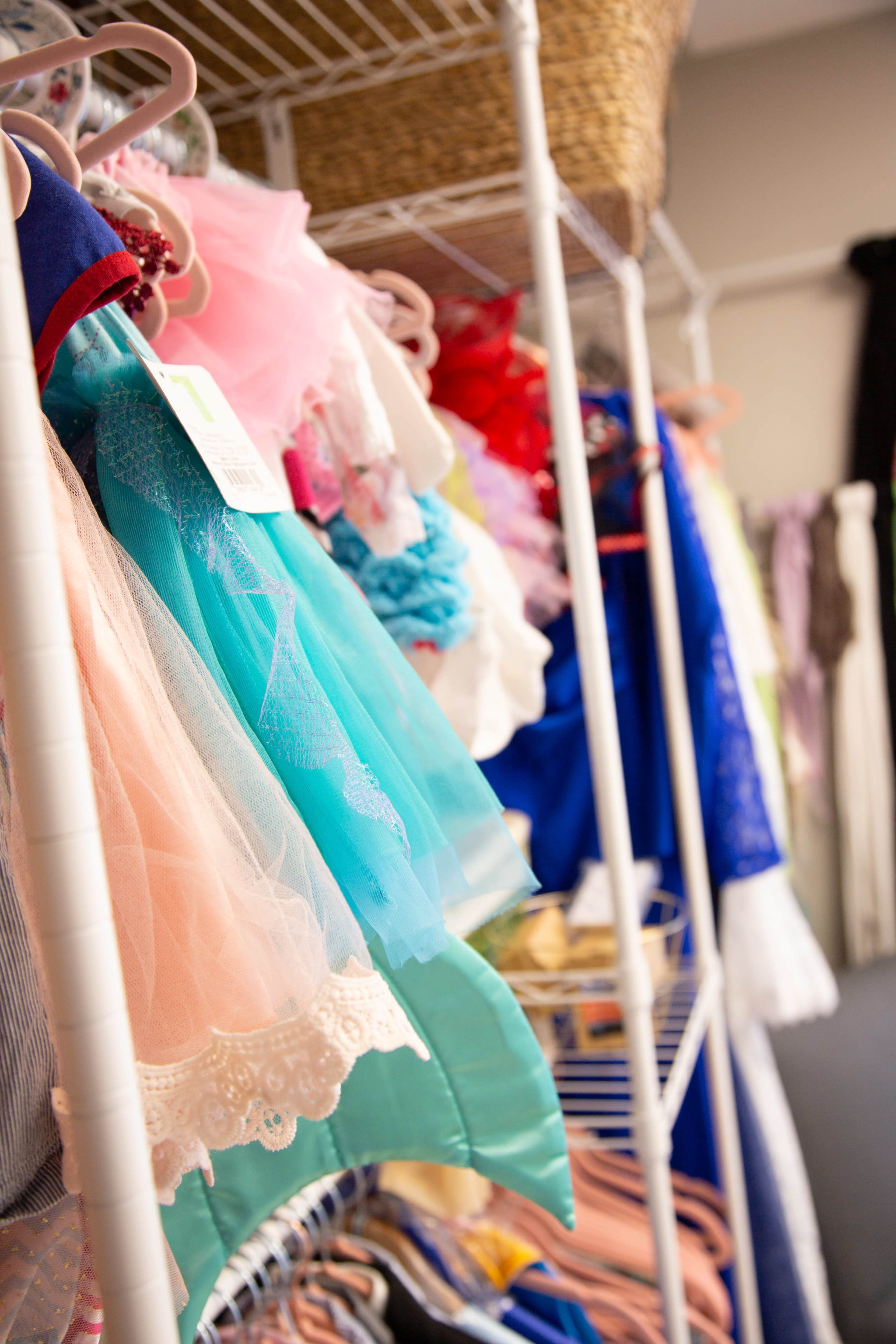 A row of colorful costumes hangs on racks in a storage area.